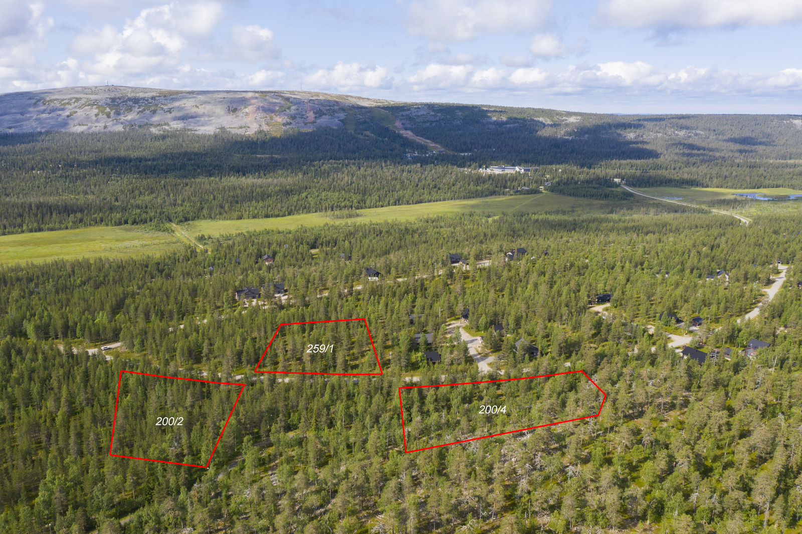 Kolmen tontin kaavat piirrettynä metsän ylle tien läheisyyteen. Taustalla kohoaa tunturi. Ilmakuva.