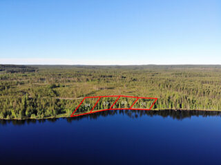 Neljän tontin kaavat piirrettynä metsään järven rannalle. Metsäalue jatkuu horisonttiin. Ilmakuva.
