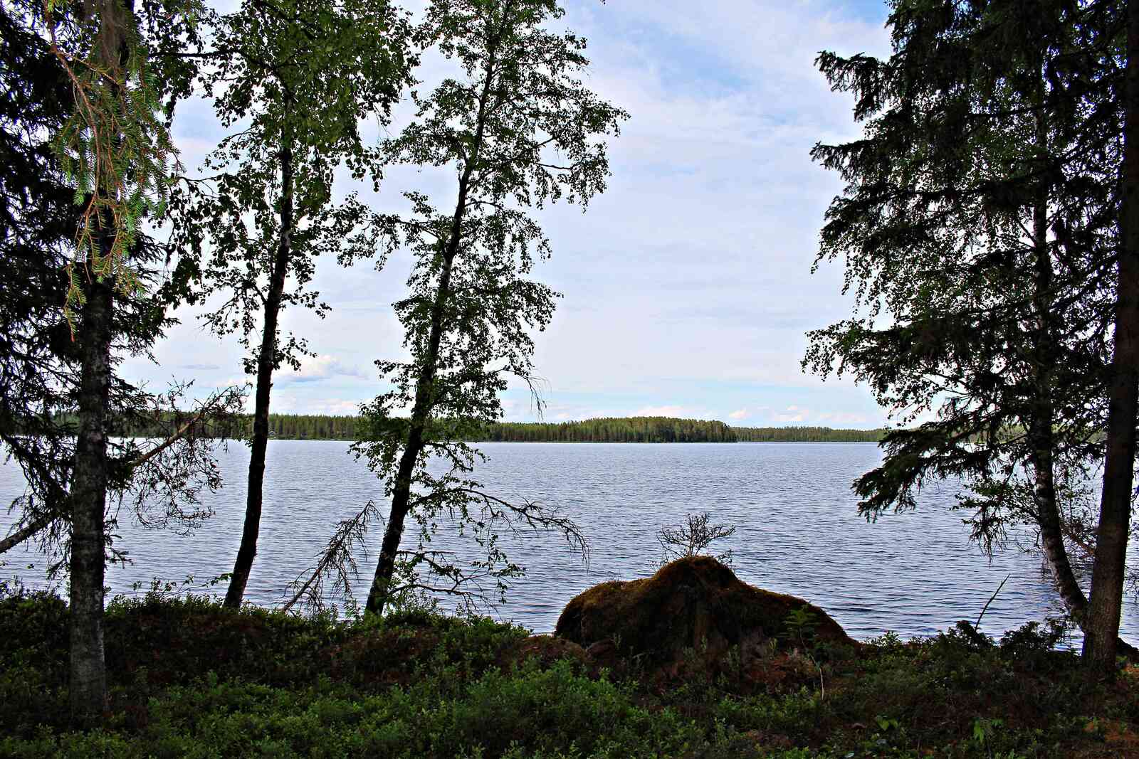Maisema järvelle, edessä on isohko kivi, vastaranta näkyy kaukaisuudessa.