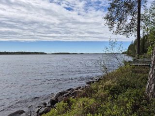 Kivikkoinen järven rantaviiva, taivaalla on pilviä, taivaanranta on pilvetön.