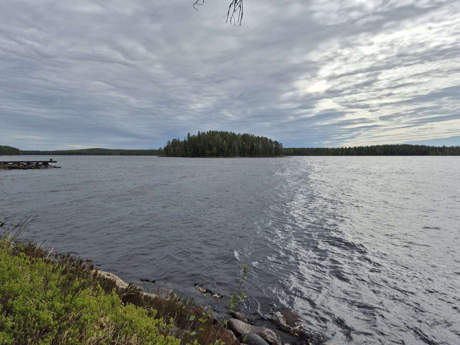 Aaltoileva järvi ja pilvinen taivas, järvellä näkyy iso saari, naapurin laituri työntyy kuvaan.