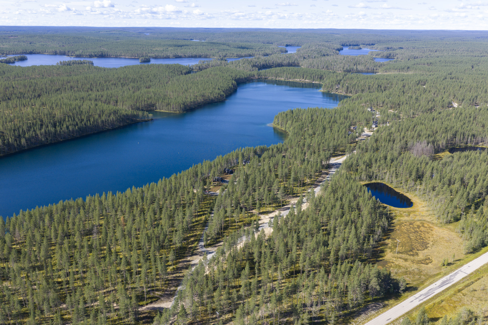Horisonttiin jatkuva metsä reunustaa järveä. Etualalla tiet risteilevät. Ilmakuva.