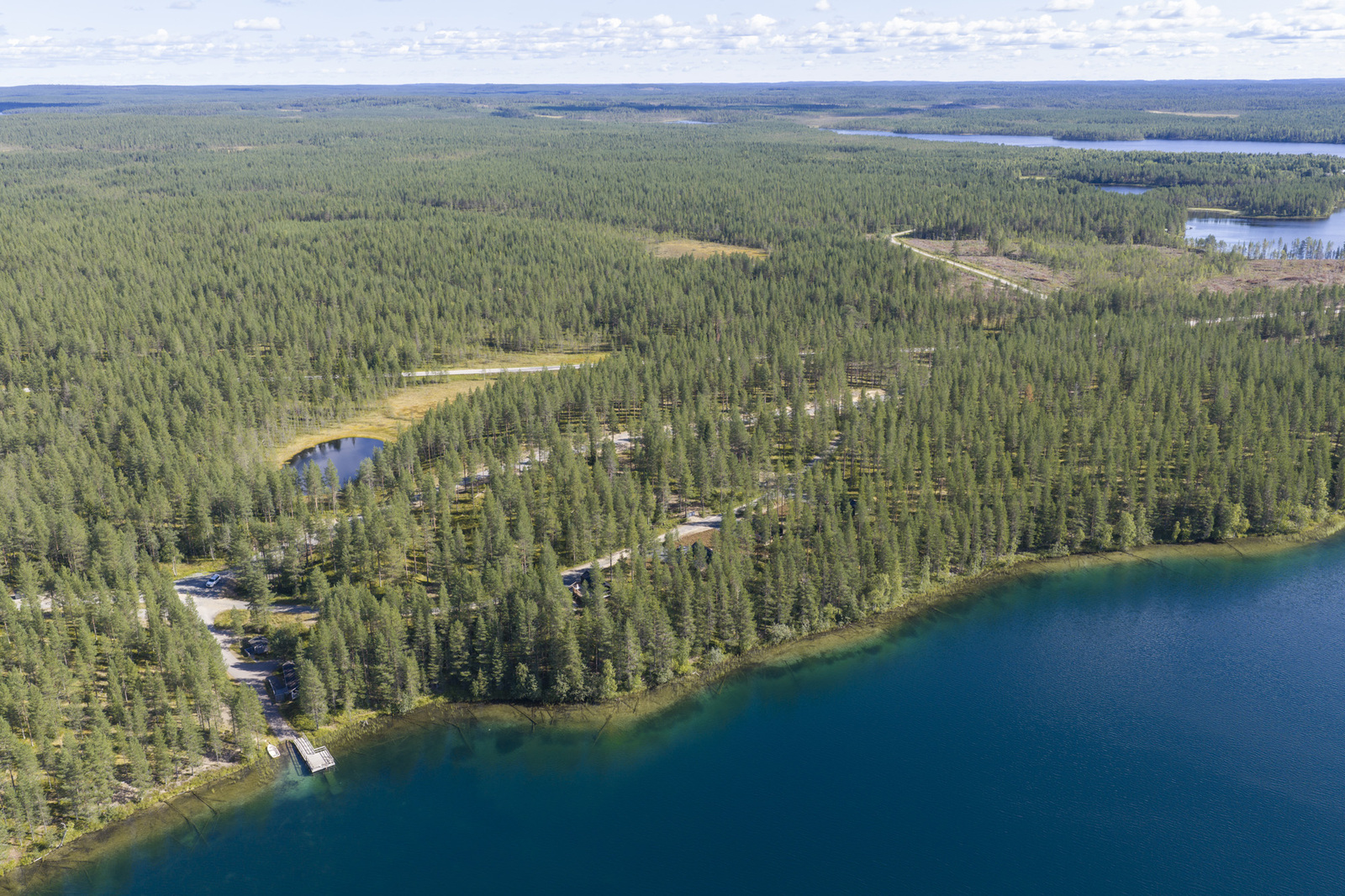 Horisonttiin jatkuva metsä reunustaa järveä. Ilmakuva järven suunnalta.