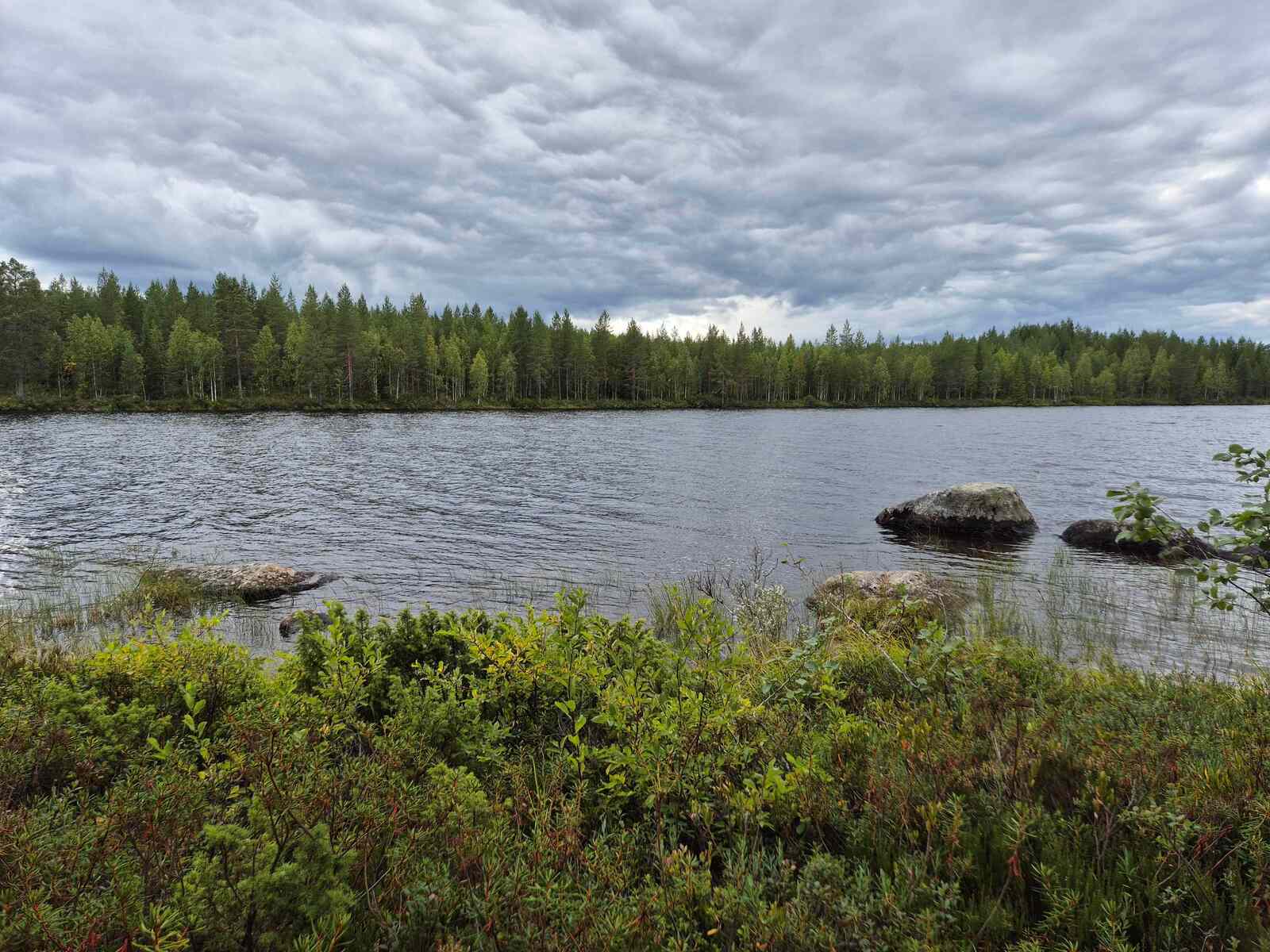 Pilvinen järvimaisema, rantavedestä kohoaa isoja kiviä.