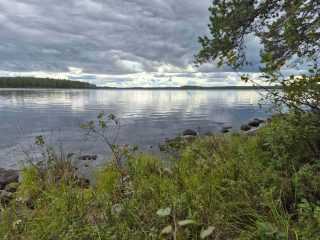 Järvimaisema, taivas on pilvinen, vesirajassa on paljon kiviä.