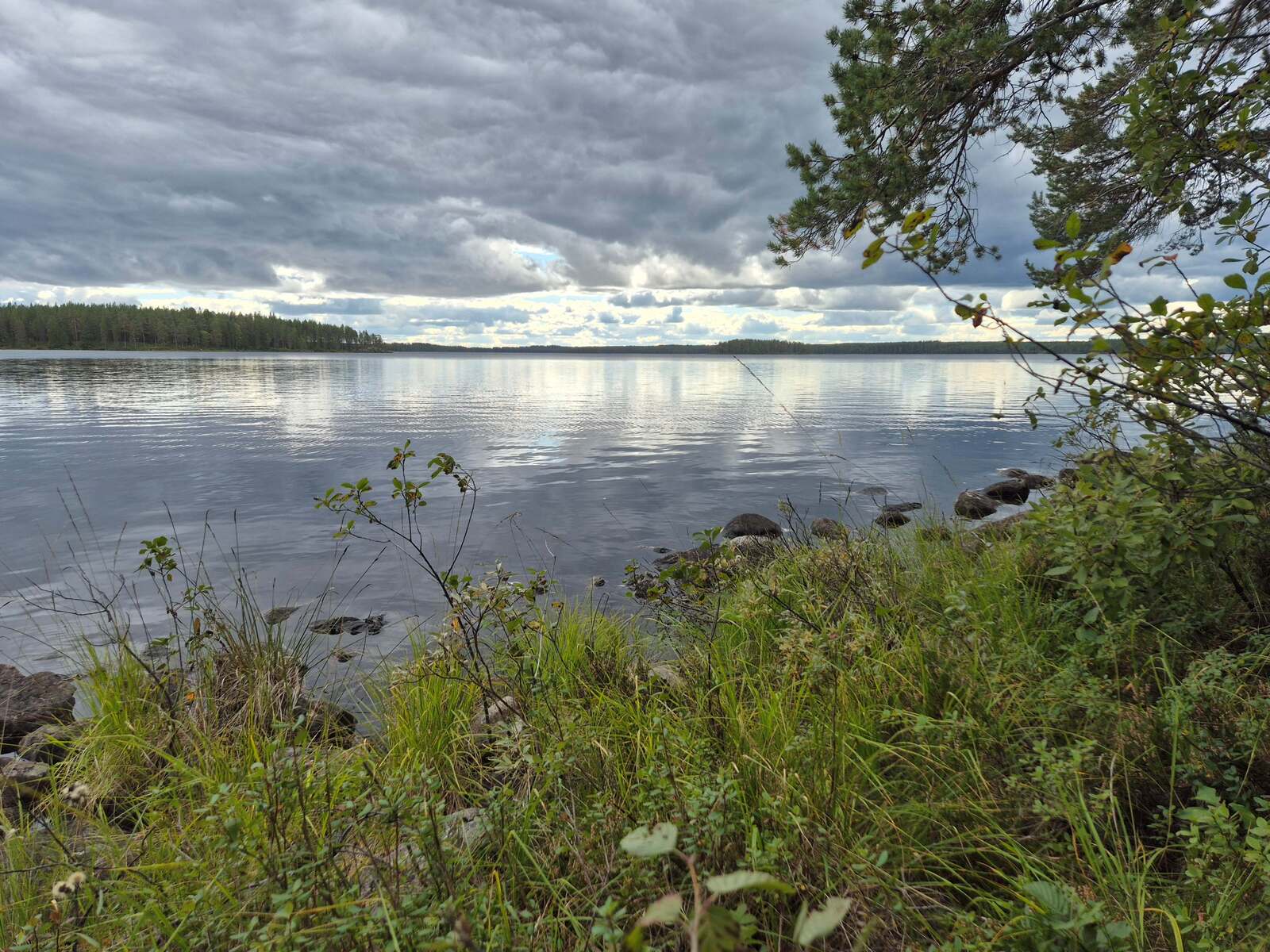 Järvimaisema, taivas on pilvinen, vesirajassa on paljon kiviä.