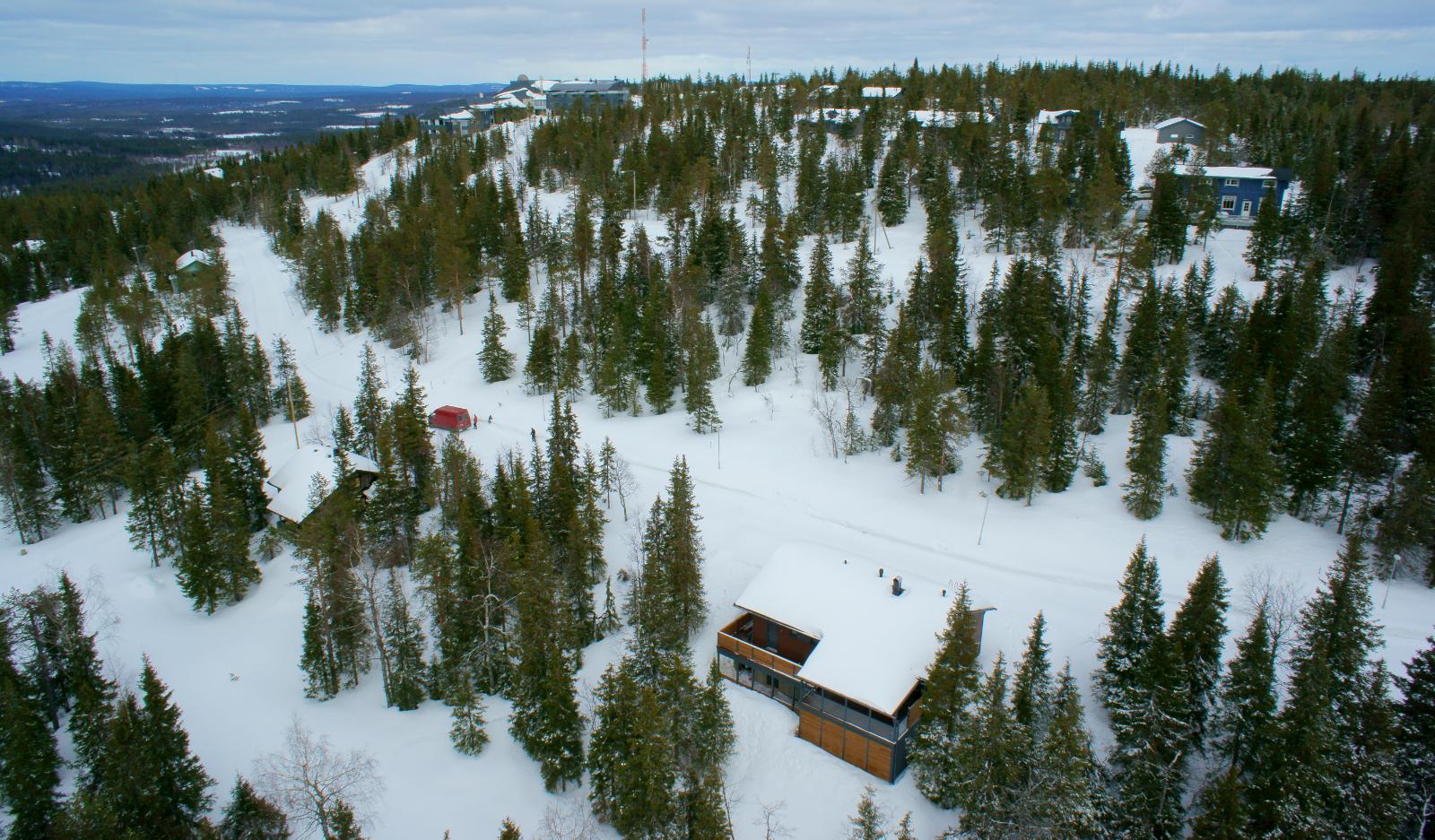 Lumipeitteisessä metsässä tunturin rinteillä on mökkejä ja huipulla hotelli. Ilmakuva.
