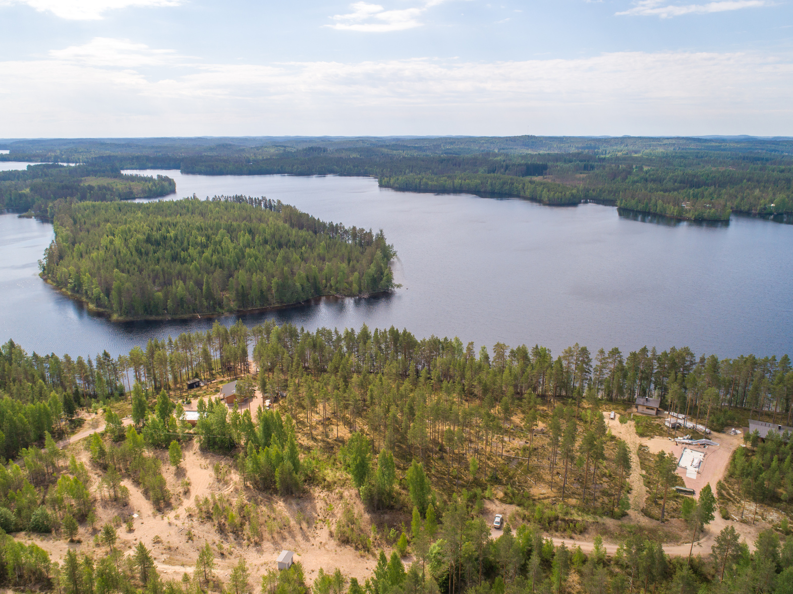 Kesämaisemassa sokkeloisen järven rannalla on mökkejä etualan metsässä. Ilmakuva.