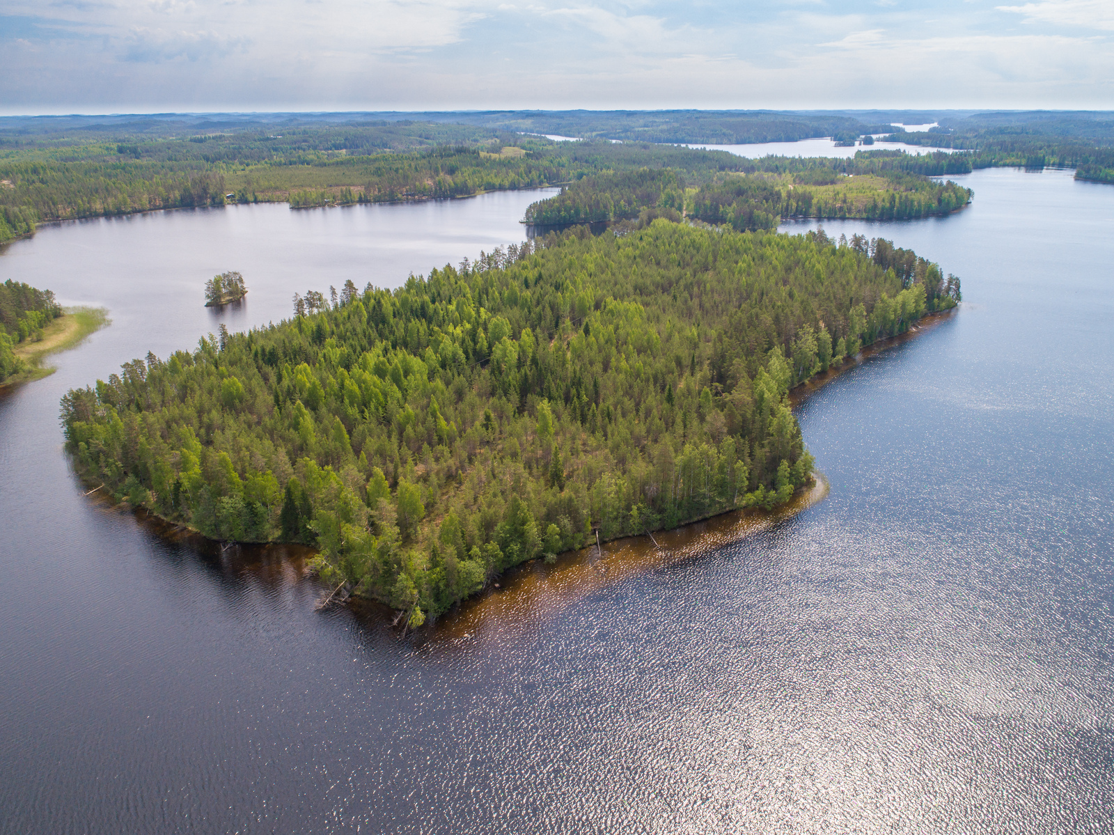 Järvessä on suuri metsäinen saari ja vesistö jatkuu horisonttiin. Ilmakuva.