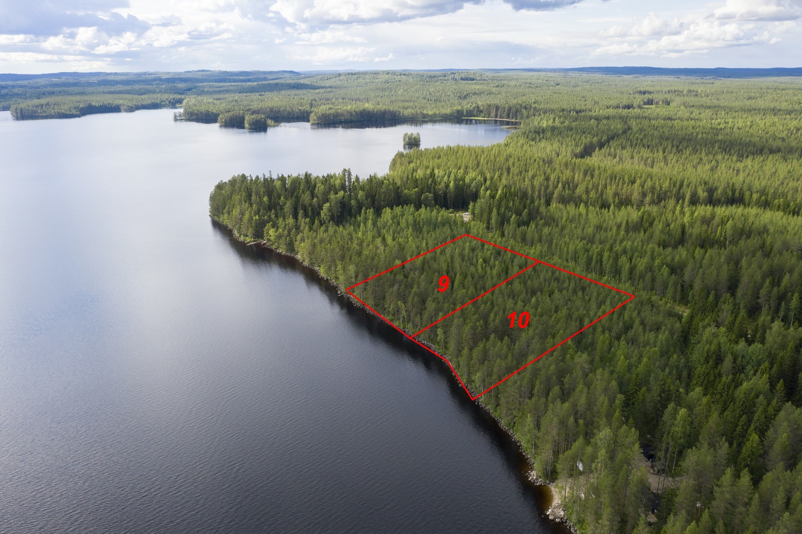 Kahden tontin kaavat piirrettynä metsän ylle järven rantaan. Järvi jatkuu horisonttiin. Ilmakuva.