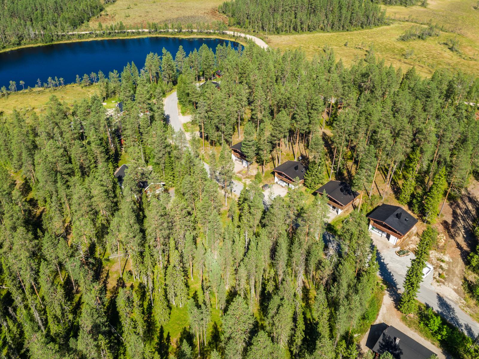 Lammelle johtavan tien varrella on lomamökkejä. Lammen takana on suo. Kesäinen ilmakuva.