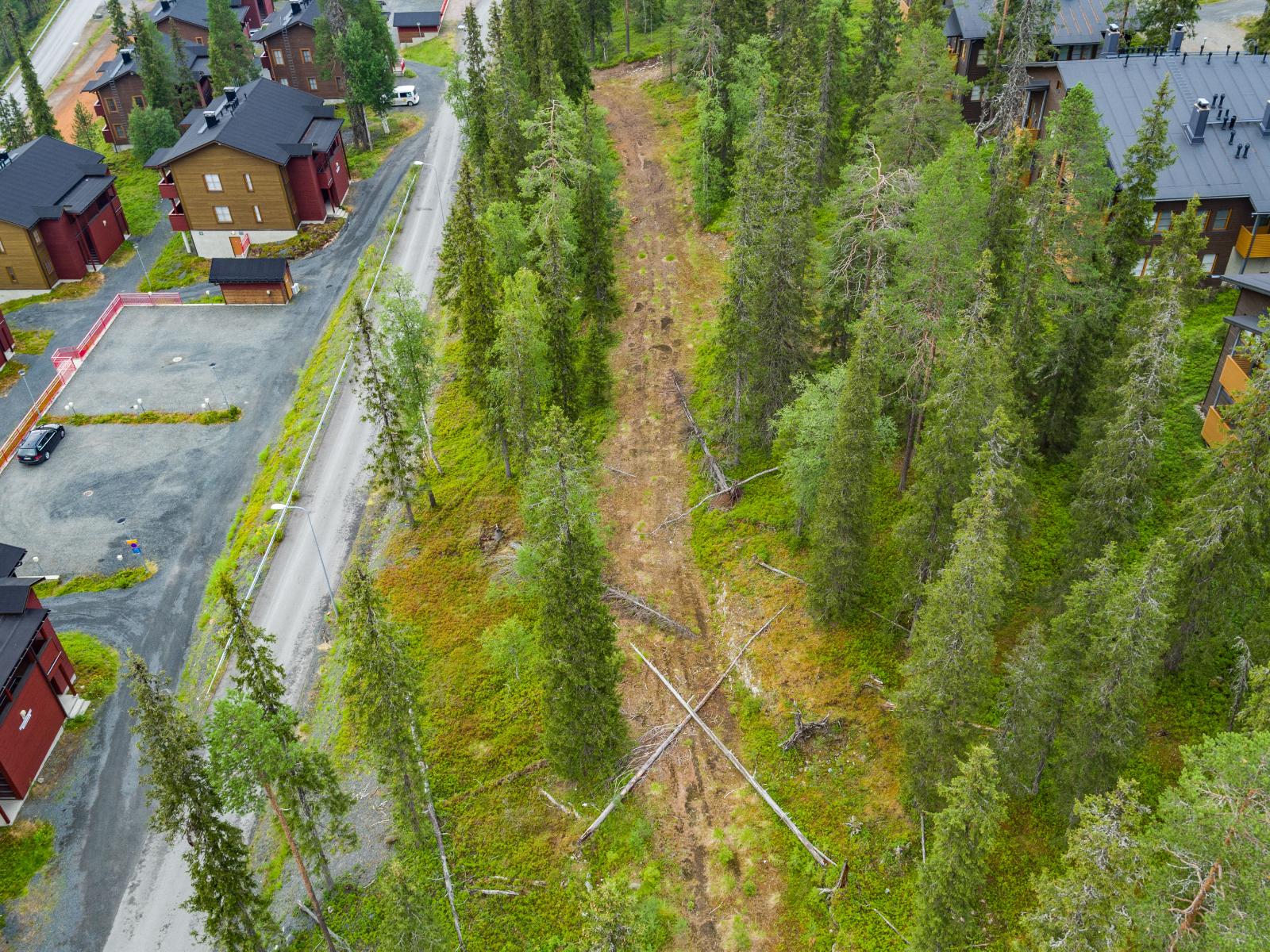 Lomahuoneistot reunustavat metsäistä kaistaletta, jonka keskellä kulkee tienpohja. Ilmakuva.