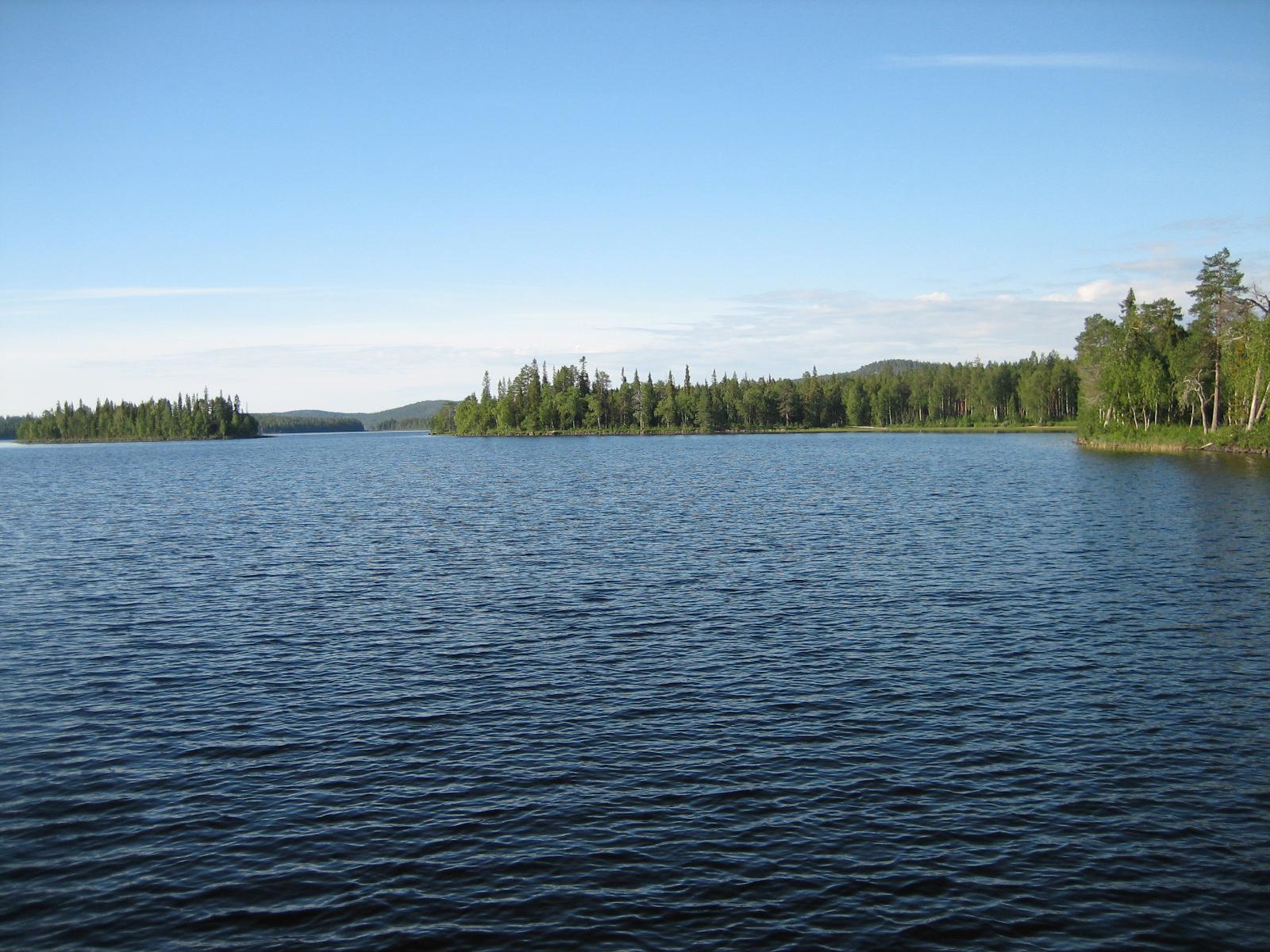 Kesäisessä järvimaisemassa vastarannalla kasvaa sekametsä ja horisontissa kohoaa vaaroja.