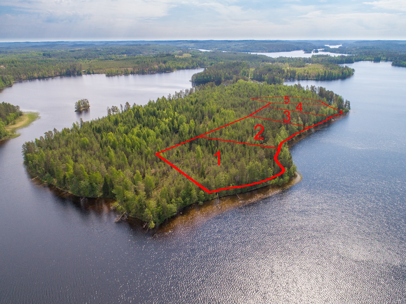 Viiden tontin kaavat piirrettynä metsäisen saaren rantaan. Järvi jatkuu horisonttiin. Ilmakuva.