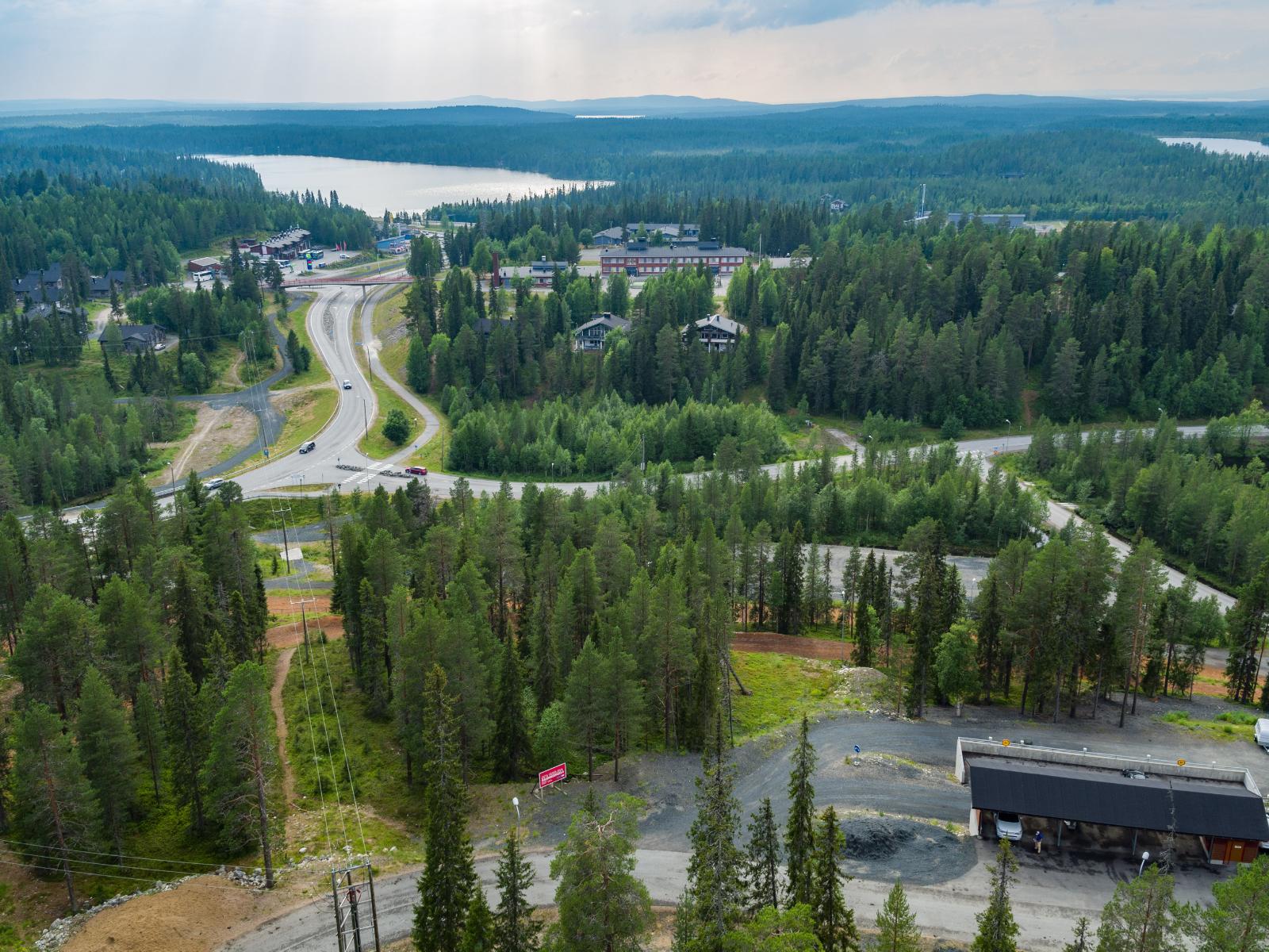 Matkailukeskusalueella risteilee teitä metsässä lomarakennusten ohi. Taustalla on järvi. Ilmakuva.