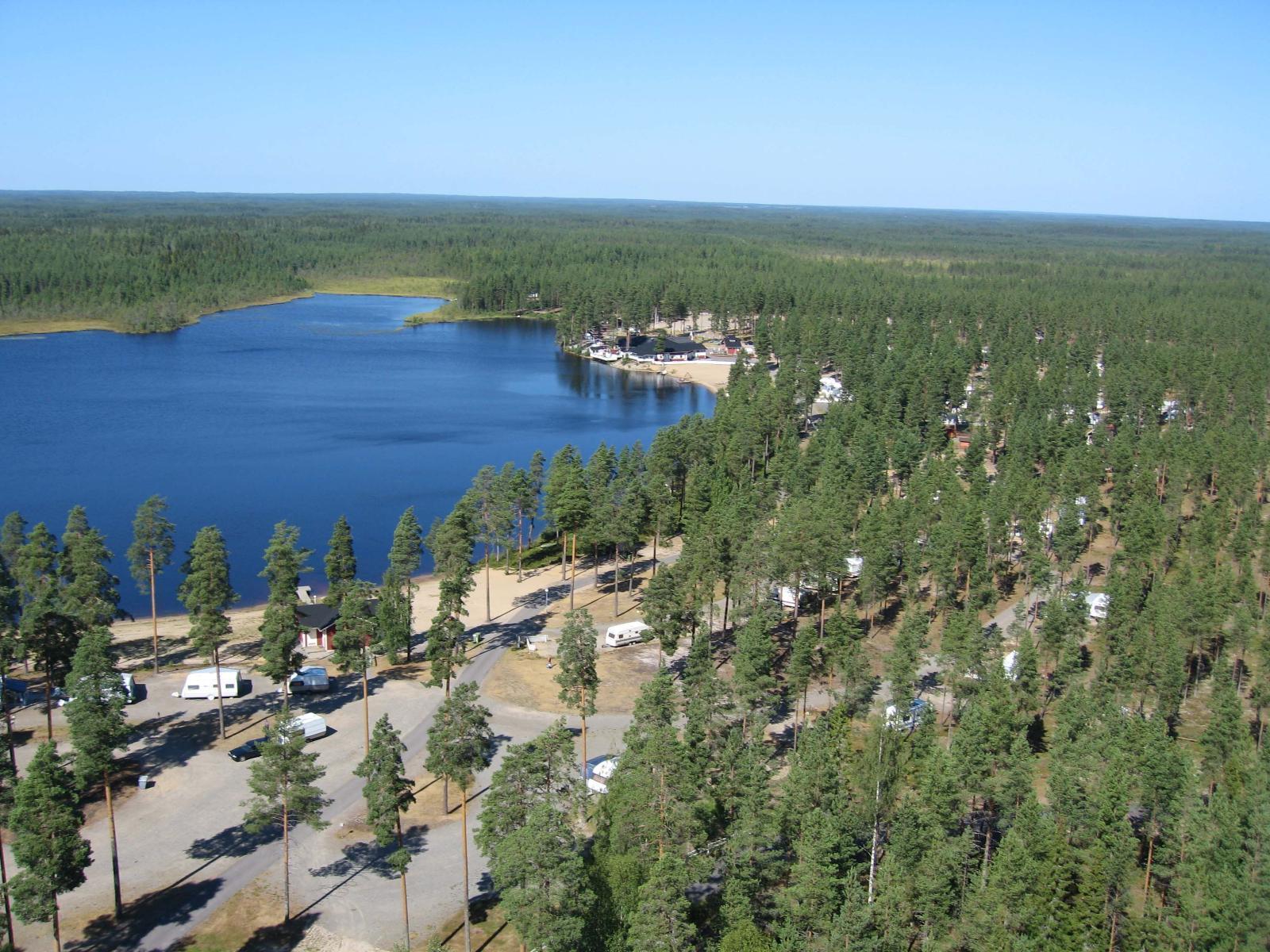 Metsät ja suot ympäröivät järveä. Etualalla on leirintäalue. Ilmakuva.