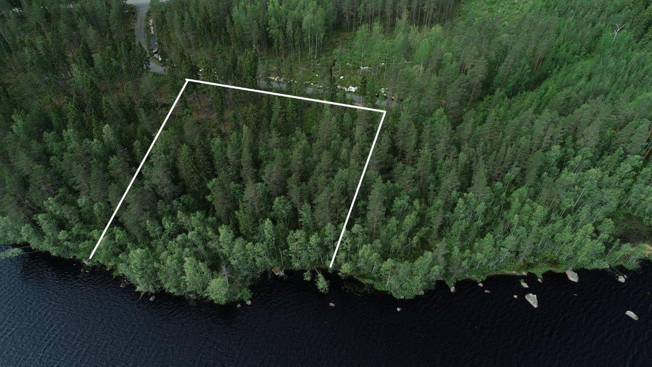 Tontin kaava piirrettynä metsään järven rantaan. Rannassa on kiviä ja tie vie tontille. Ilmakuva.