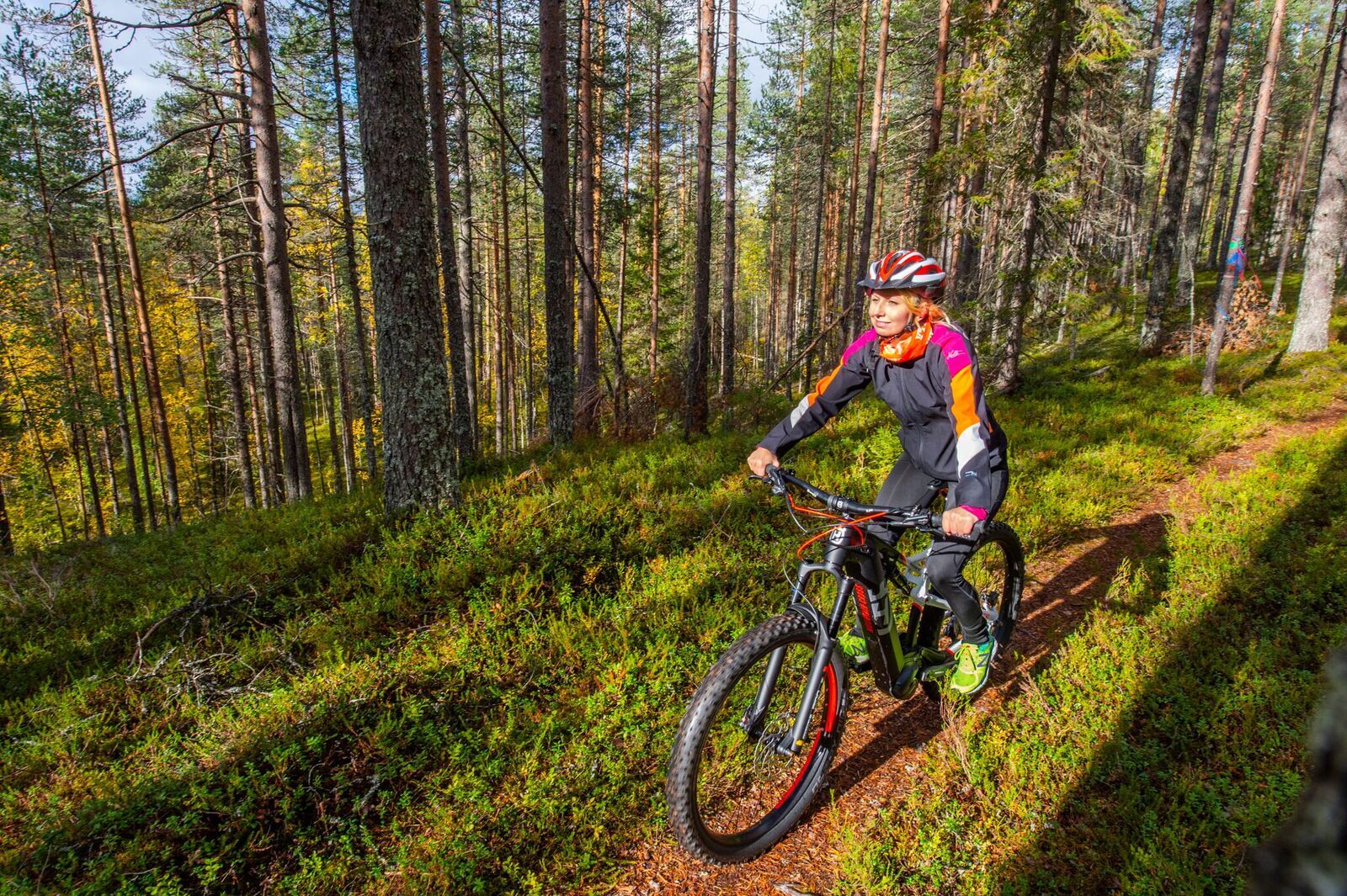 Hymyilevä maastopyöräilijä polkee merkityllä reitillä valoisassa metsässä.