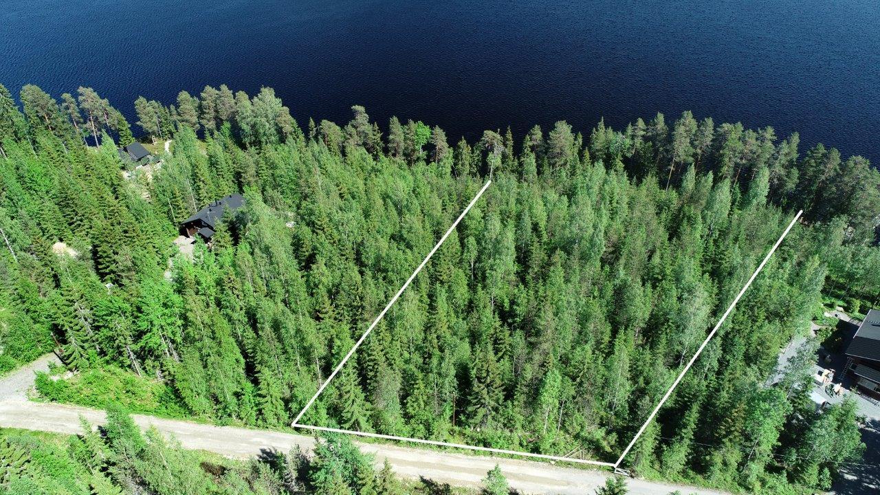 Tontin kaava piirrettynä kesäisen metsän ylle järven rantaan. Vieressä on naapurimökki. Ilmakuva.