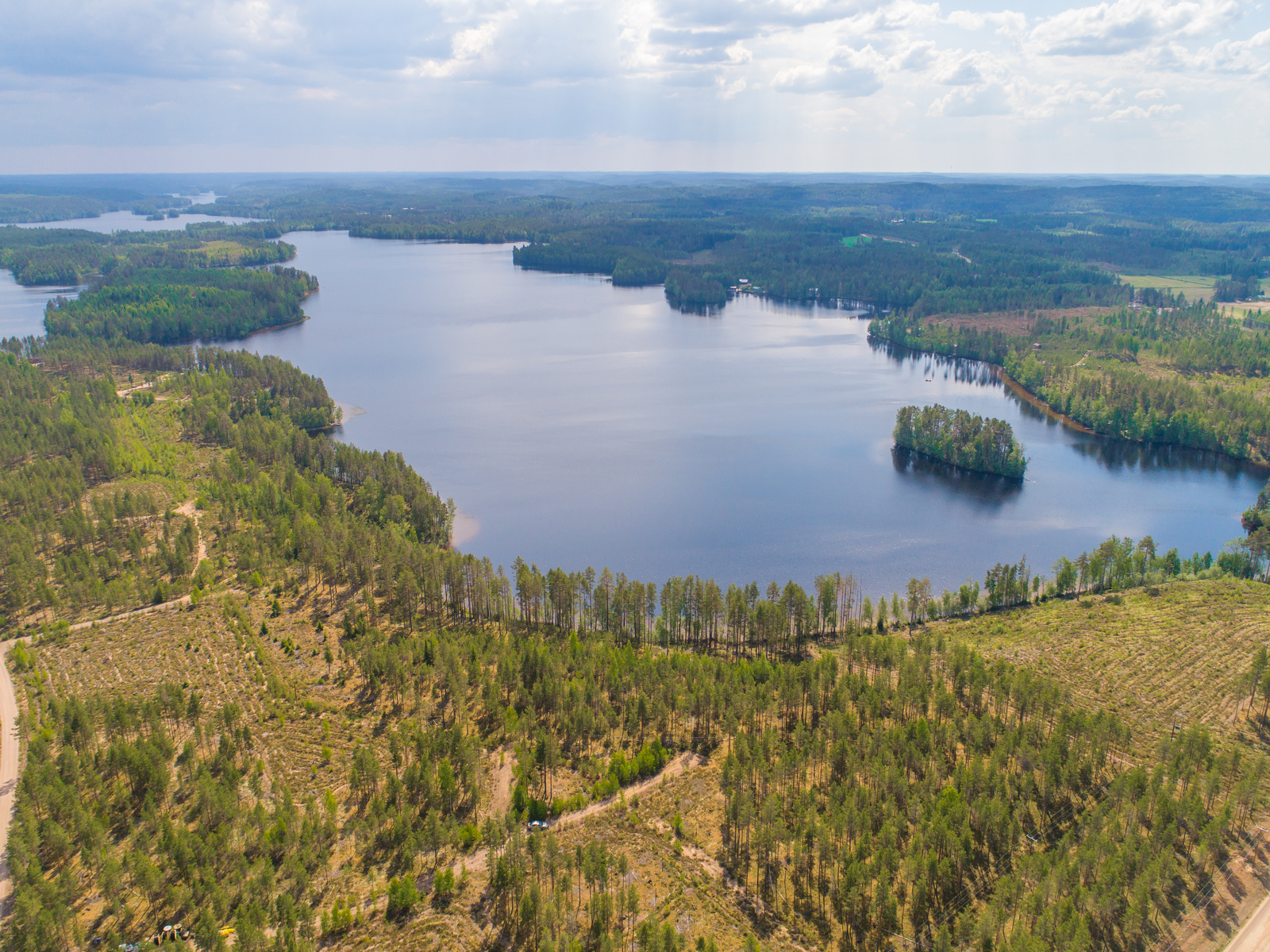 Metsiköt reunustavat pitkulaista ja sokkeloista järveä. Etualalla hakkuuaukeita. Ilmakuva.