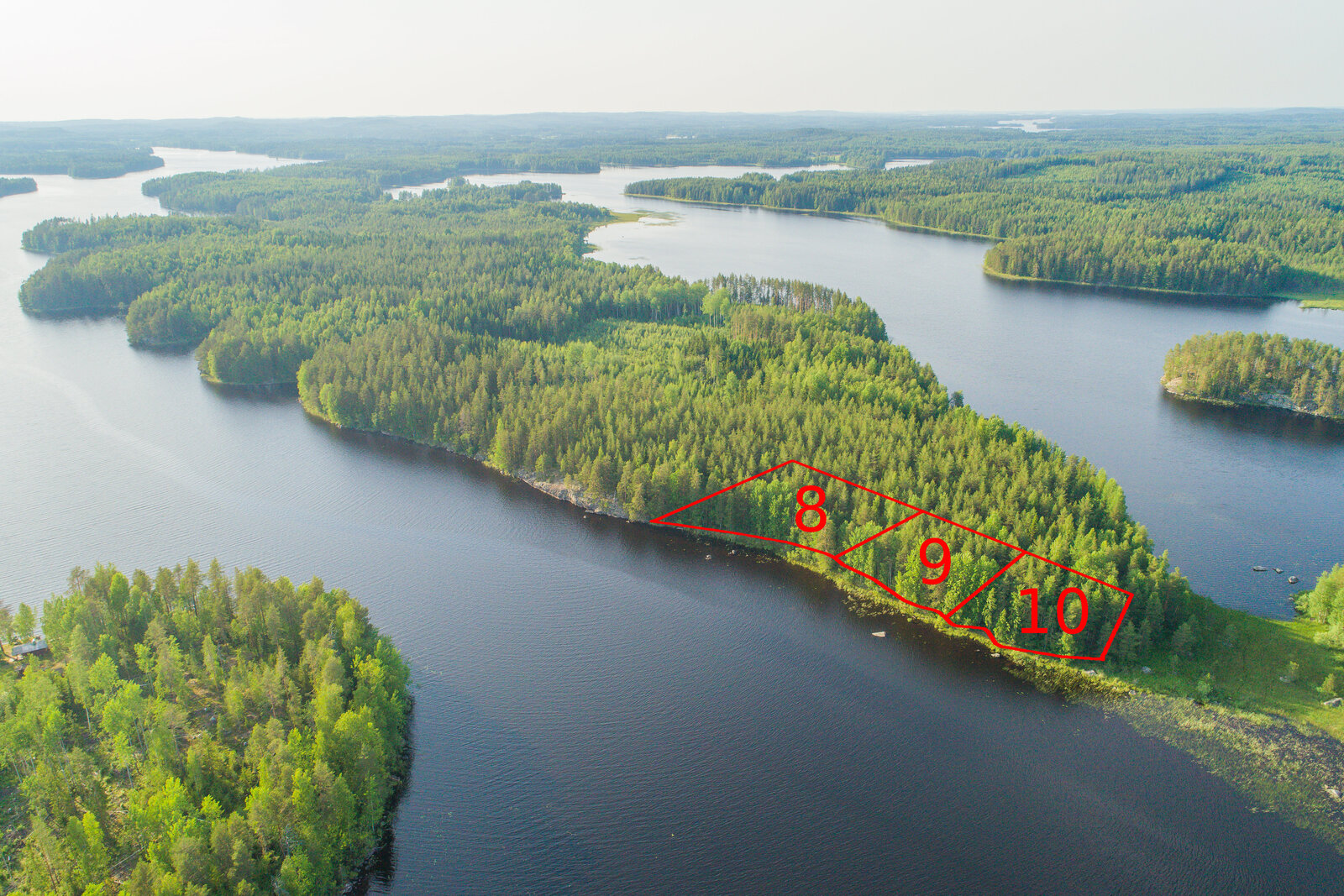 Vesistö ympäröi metsäistä saarta, jonka rantaan on piirretty kolmen tontin kaavat. Ilmakuva.