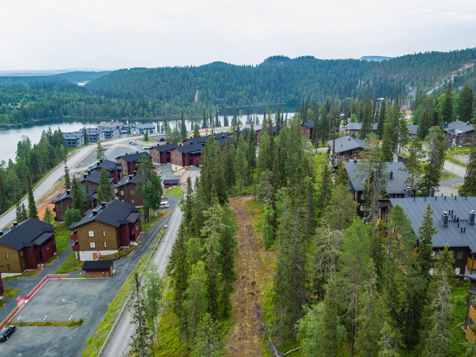 Tunturi- ja vaaramaiseman edustalla on järvi sekä matkailukeskuksen rakennuksia. Ilmakuva.