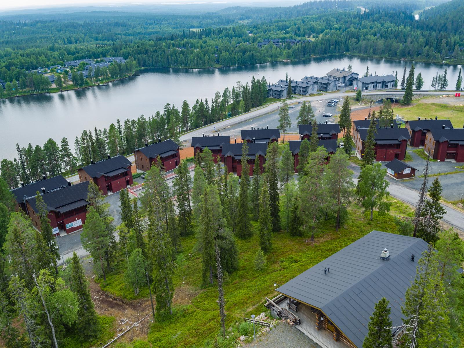 Järven läheisyydessä on lomahuoneistoja. Etualalla on havupuita kasvava tontti. Ilmakuva.