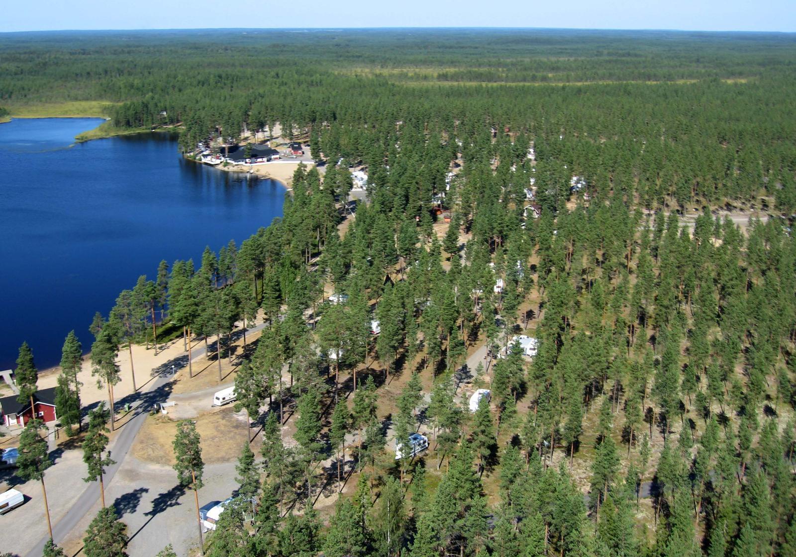 Järven rannalla on leirintäalue, jota ympäröi kauas ulottuva mäntymetsä. Ilmakuva.