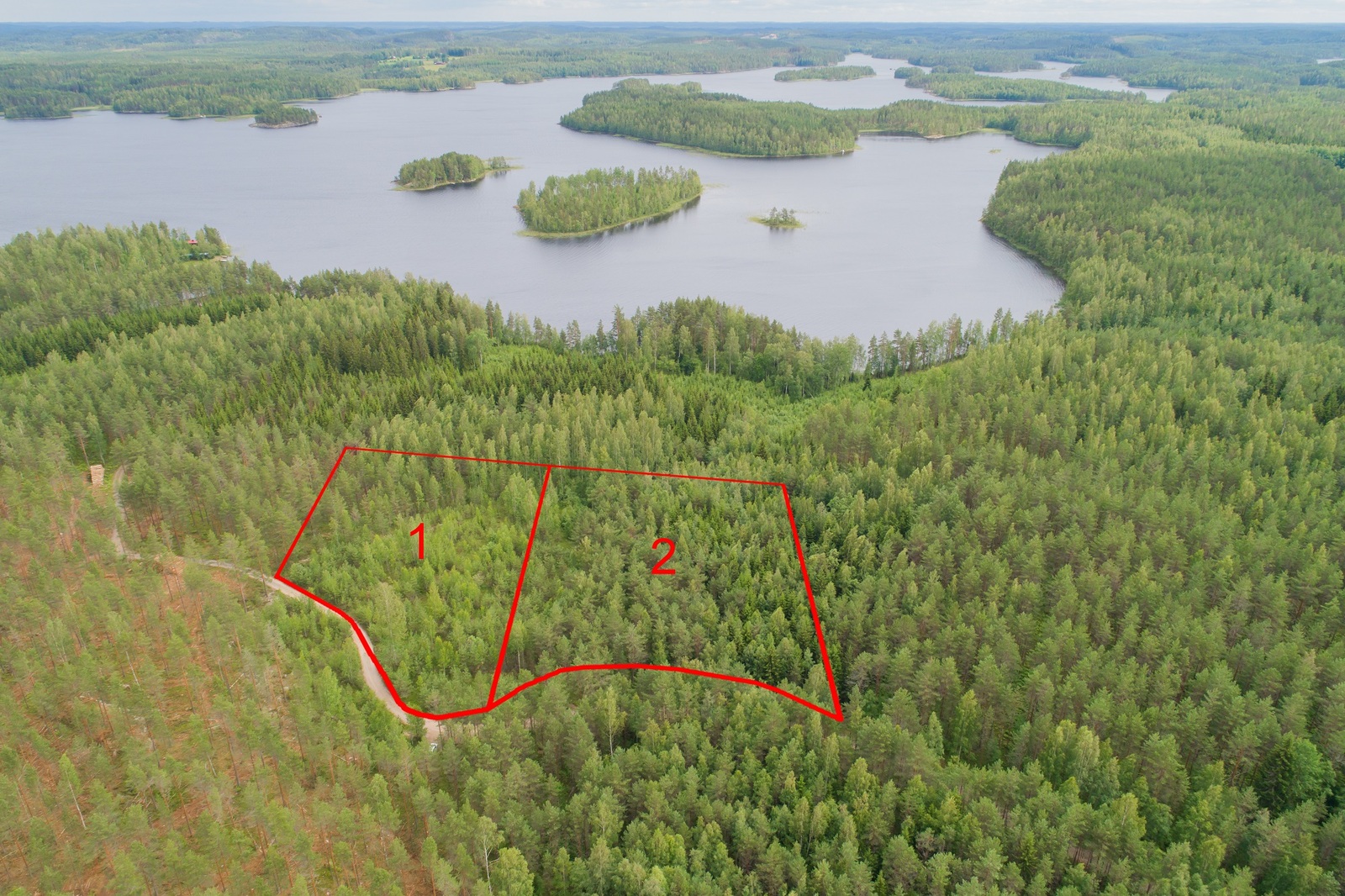 Ilmakuvassa piirrettynä kahden tontin kaavat tien varteen. Metsäalueita reunustaa ylälaidassa järvi.