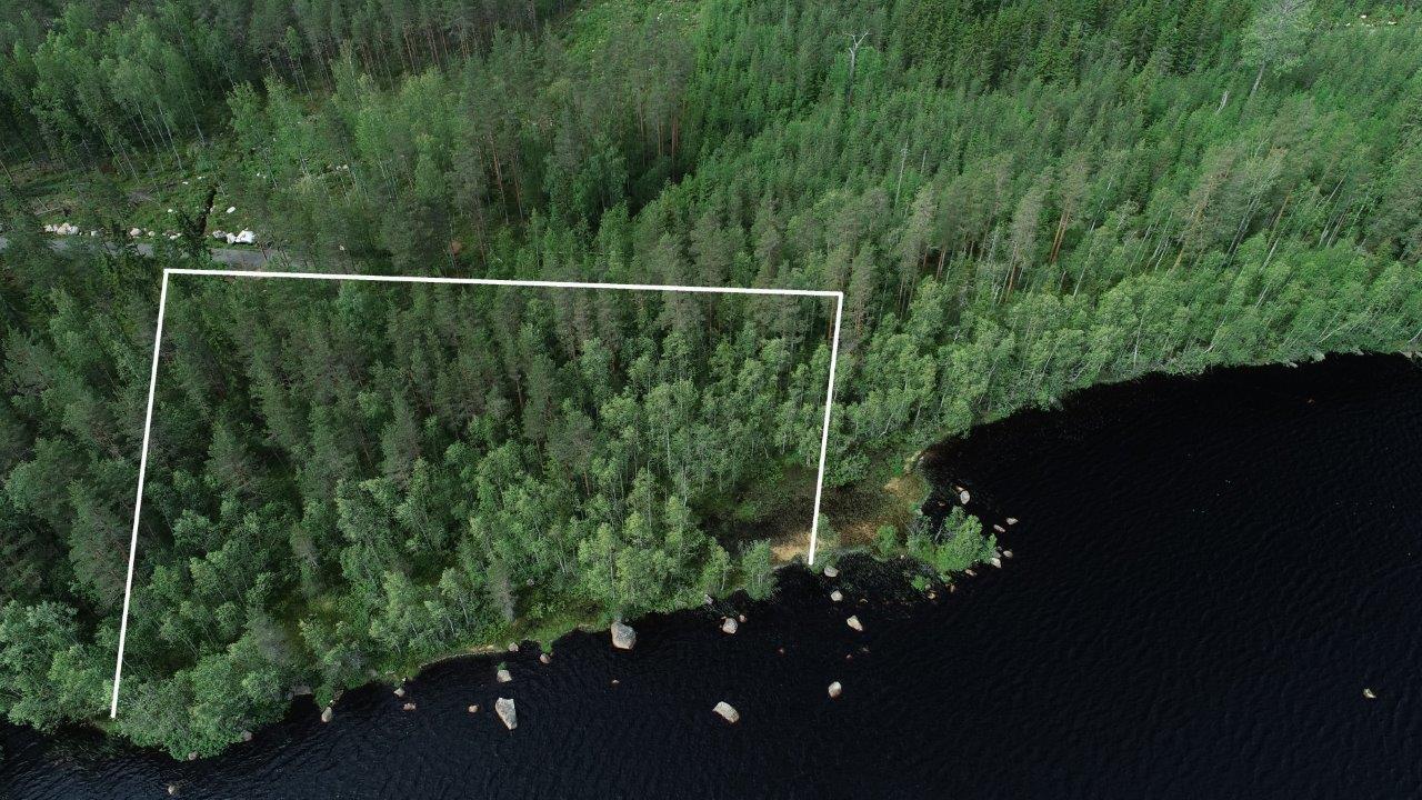 Tontin kaava piirrettynä metsään järven rantaan. Rannassa on kiviä ja tie vie tontille. Ilmakuva.