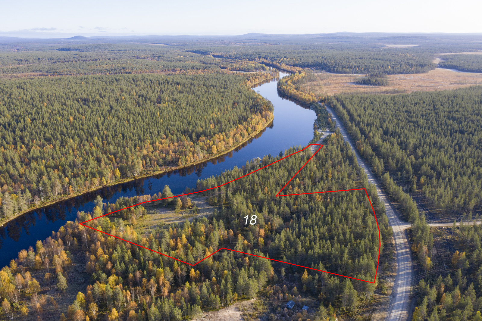 Tontin kaava piirrettynä joen ja tien väliin. Laaja syksyinen metsä jatkuu horisonttiin. Ilmakuva.