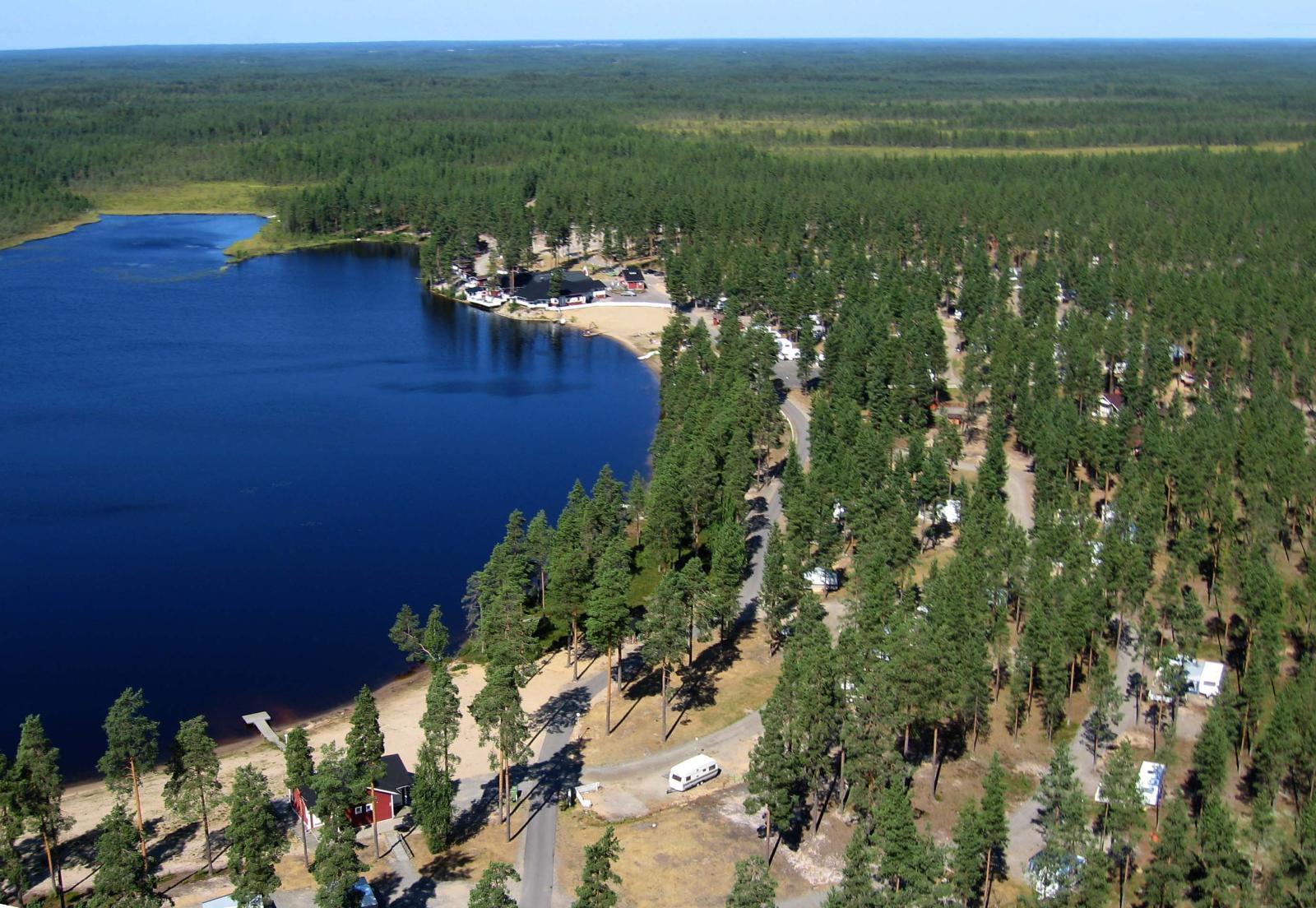 Järven rannalla on leirintäalue, jota ympäröi kauas ulottuva mäntymetsä. Ilmakuva.