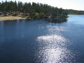 Järven vastarannalla on hiekkaranta ja leirintäalue. Vedenpinnassa heijastuu auringonvalo. Ilmakuva.