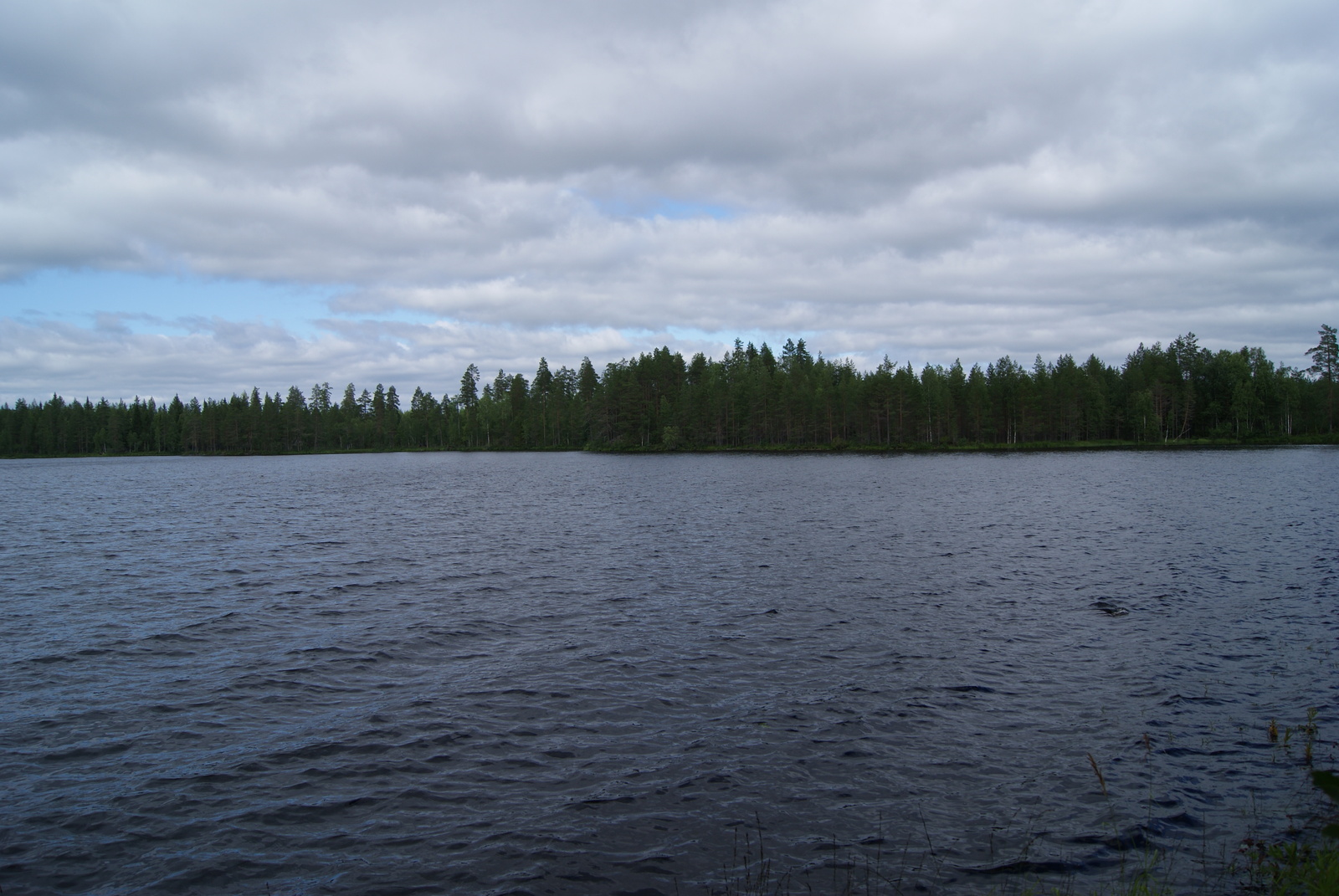 Järvimaisemassa veden pinta laineilee hieman ja taivaalla on pilviä.