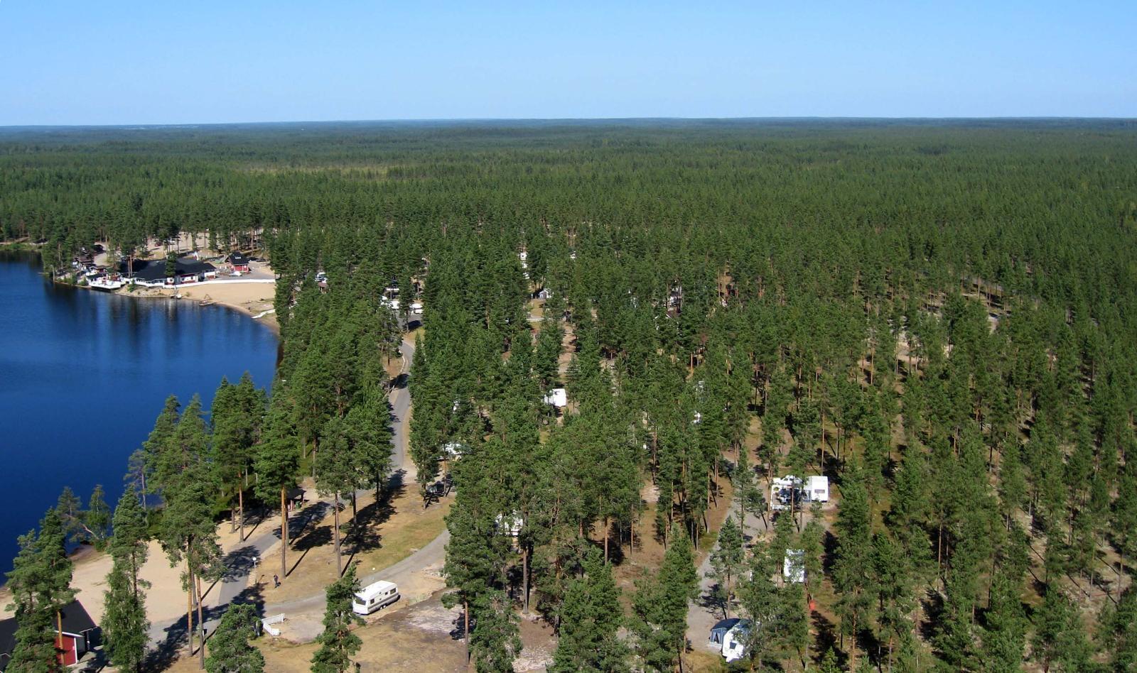 Metsät ja suot ympäröivät järveä. Etualalla on leirintäalue, jota ympäröi laaja metsä. Ilmakuva.