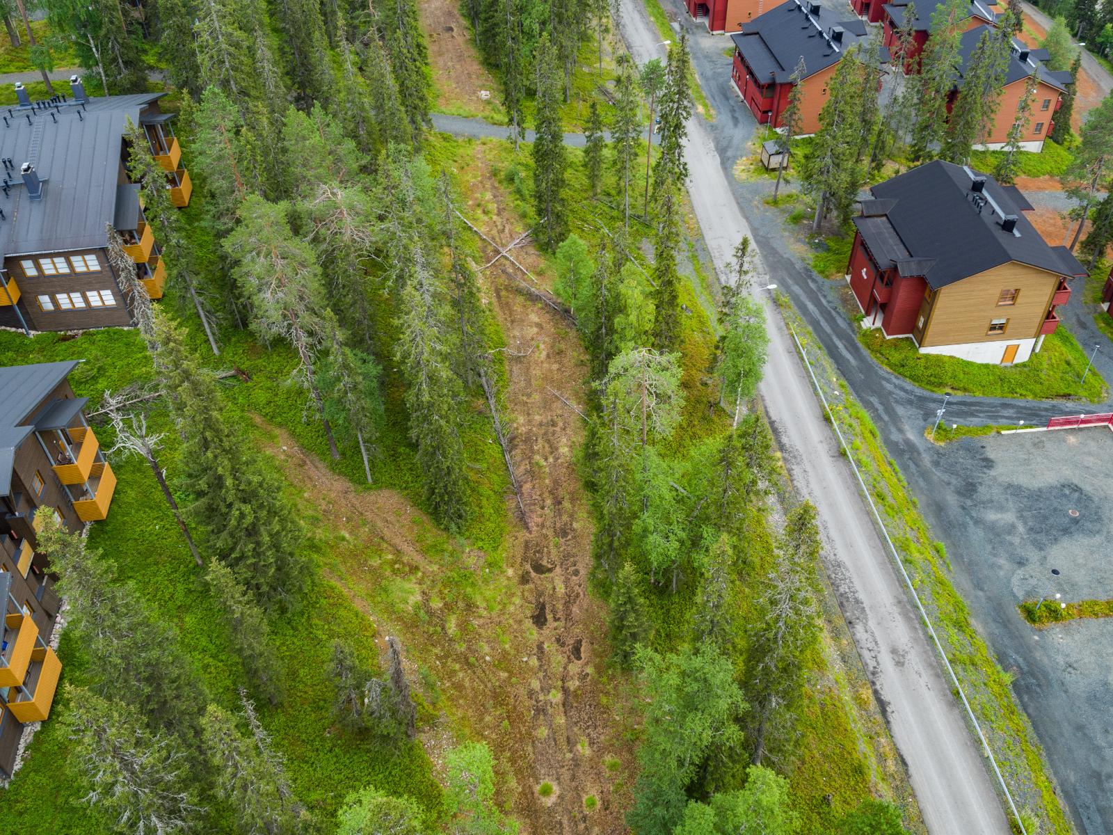 Lomahuoneistot reunustavat metsäistä kaistaletta, jonka keskellä kulkee tienpohja. Ilmakuva.