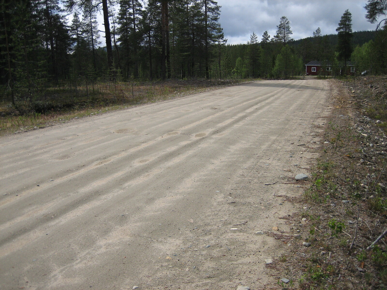 Metsässä kulkevan hiekkatien varrella on rakennus.