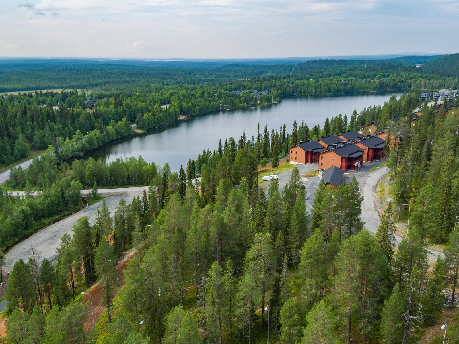 Järven tuntumassa on lomarakennuksia ja taustalla metsäalue jatkuu horisonttiin. Ilmakuva.