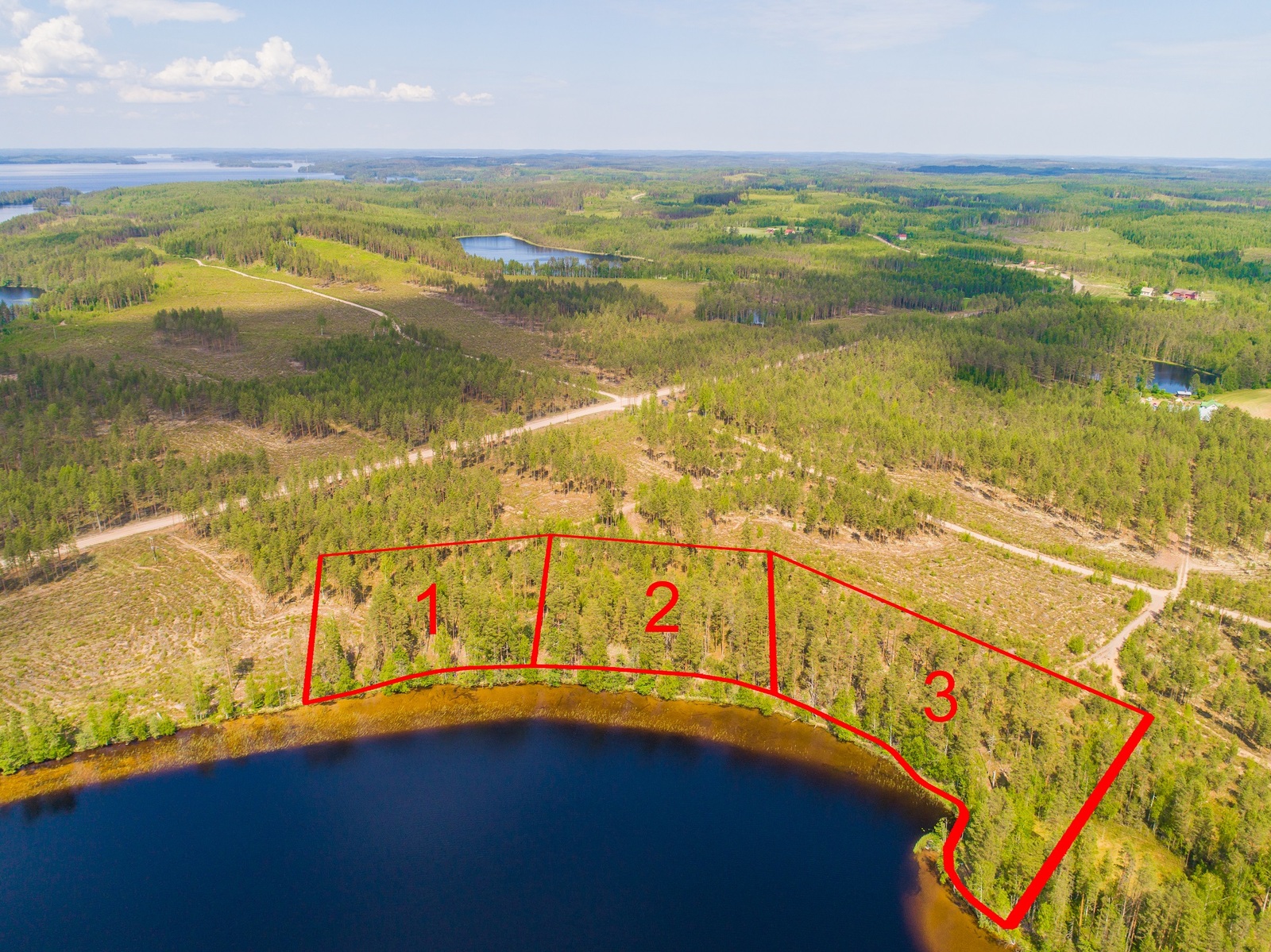 Kolmen tontin kaavat piirrettynä metsään järven rantaan. Ilmakuva.