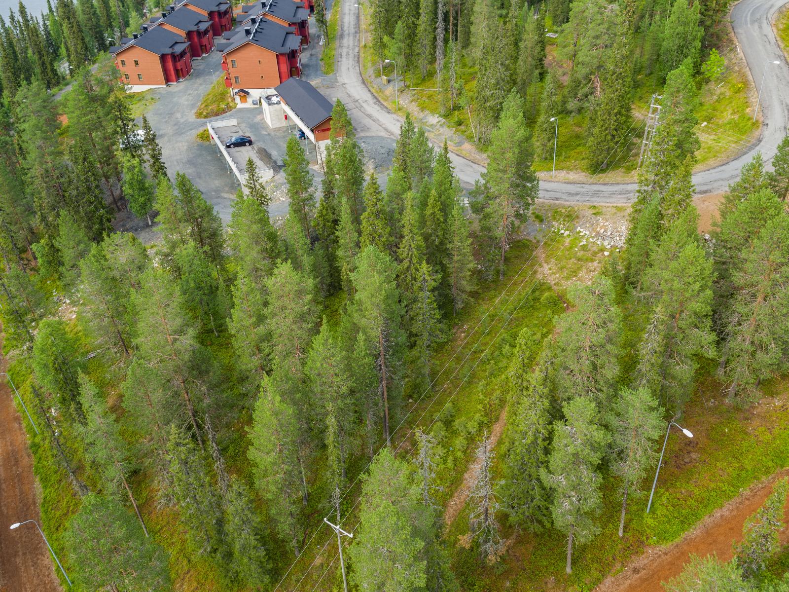 Tie tekee mutkan lomahuoneistojen ohi. Etualalla sähkölinja kulkee havumetsässä. Ilmakuva.