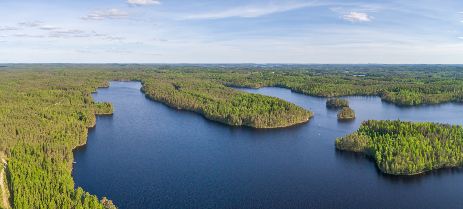 Kesämaisemassa metsien reunustama järvi jatkuu moneen eri suuntaan ja siinä on saaria. Ilmakuva.