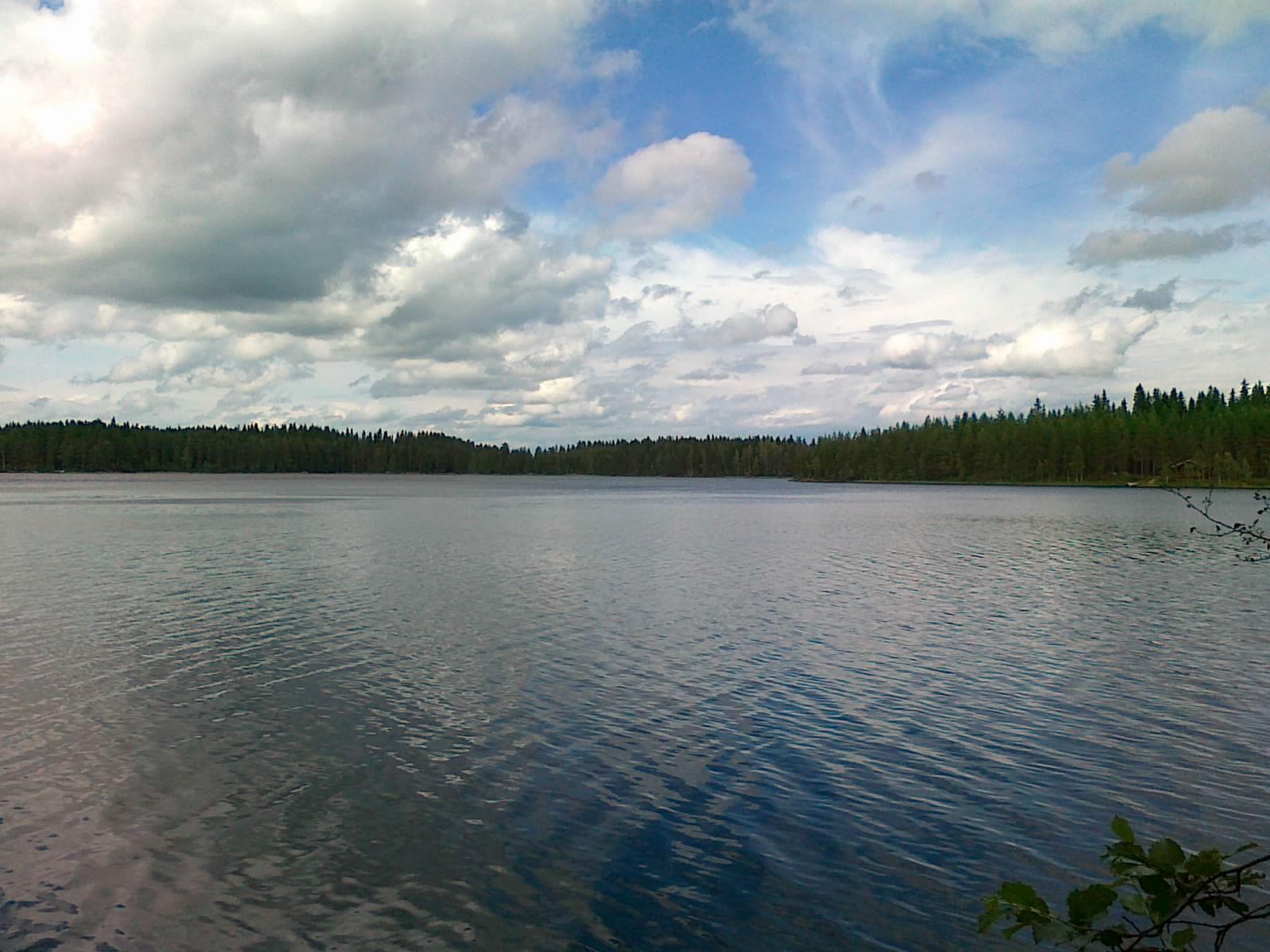 Poutapilvinen taivas heijastuu hieman väreilevään veden pintaan järvimaisemassa.