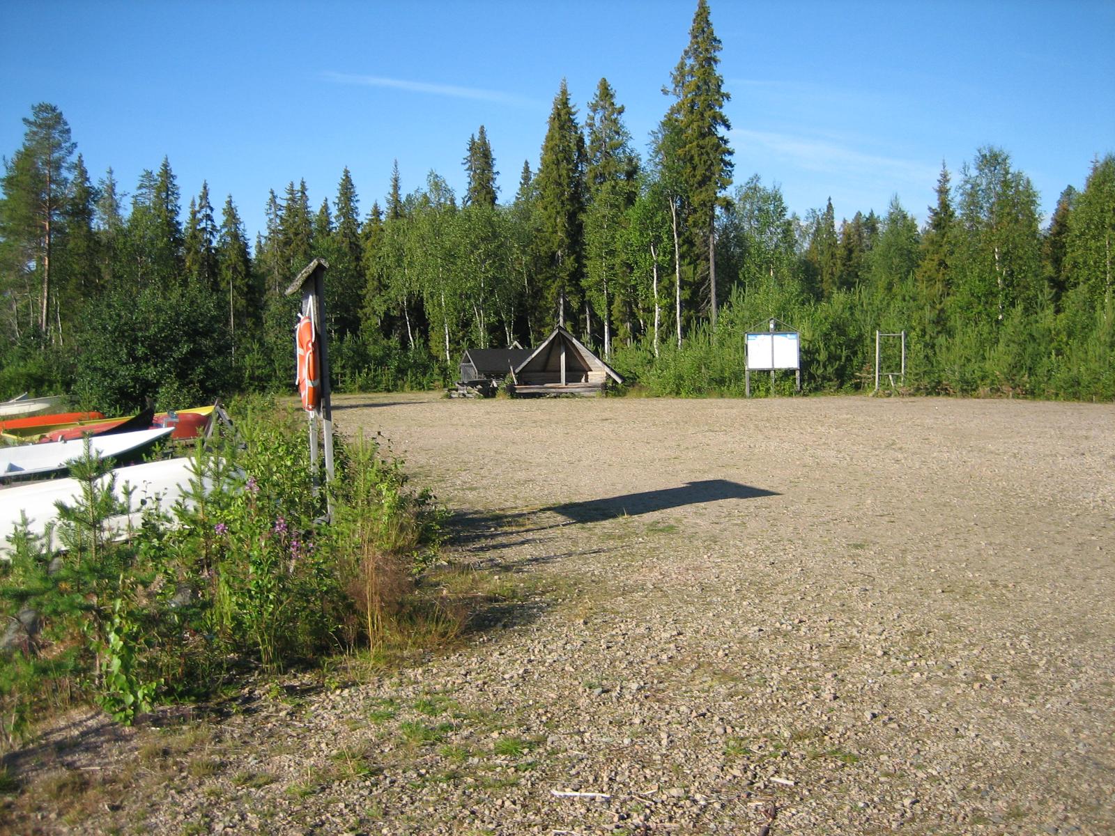 Etualalla veneenlaskupaikan pysäköintialue, jonka takana on laavu ja metsää. Vasemmalla veneitä.