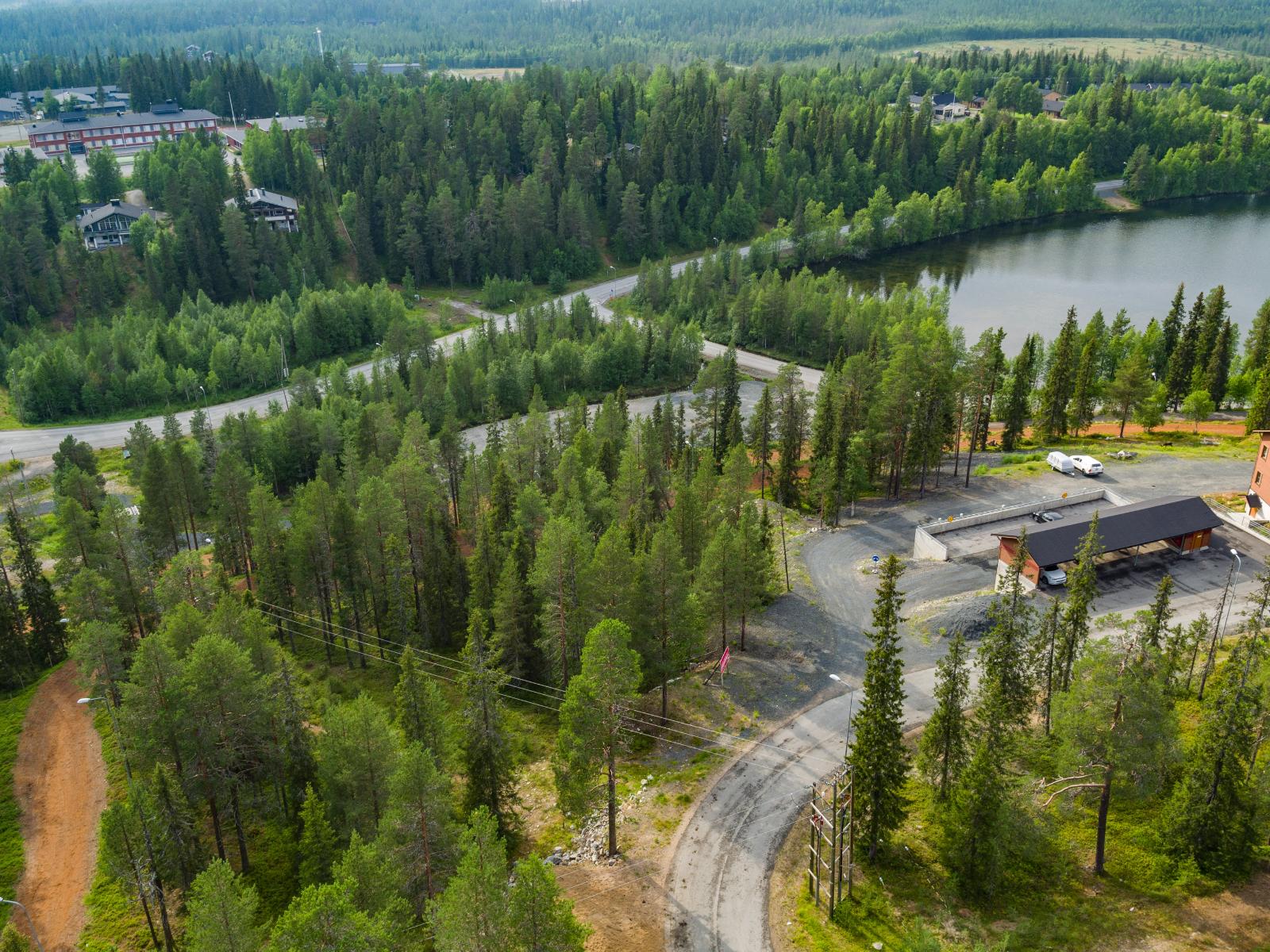 Matkailukeskusalueella risteilee teitä metsässä lomarakennusten ja järven ohi. Ilmakuva.