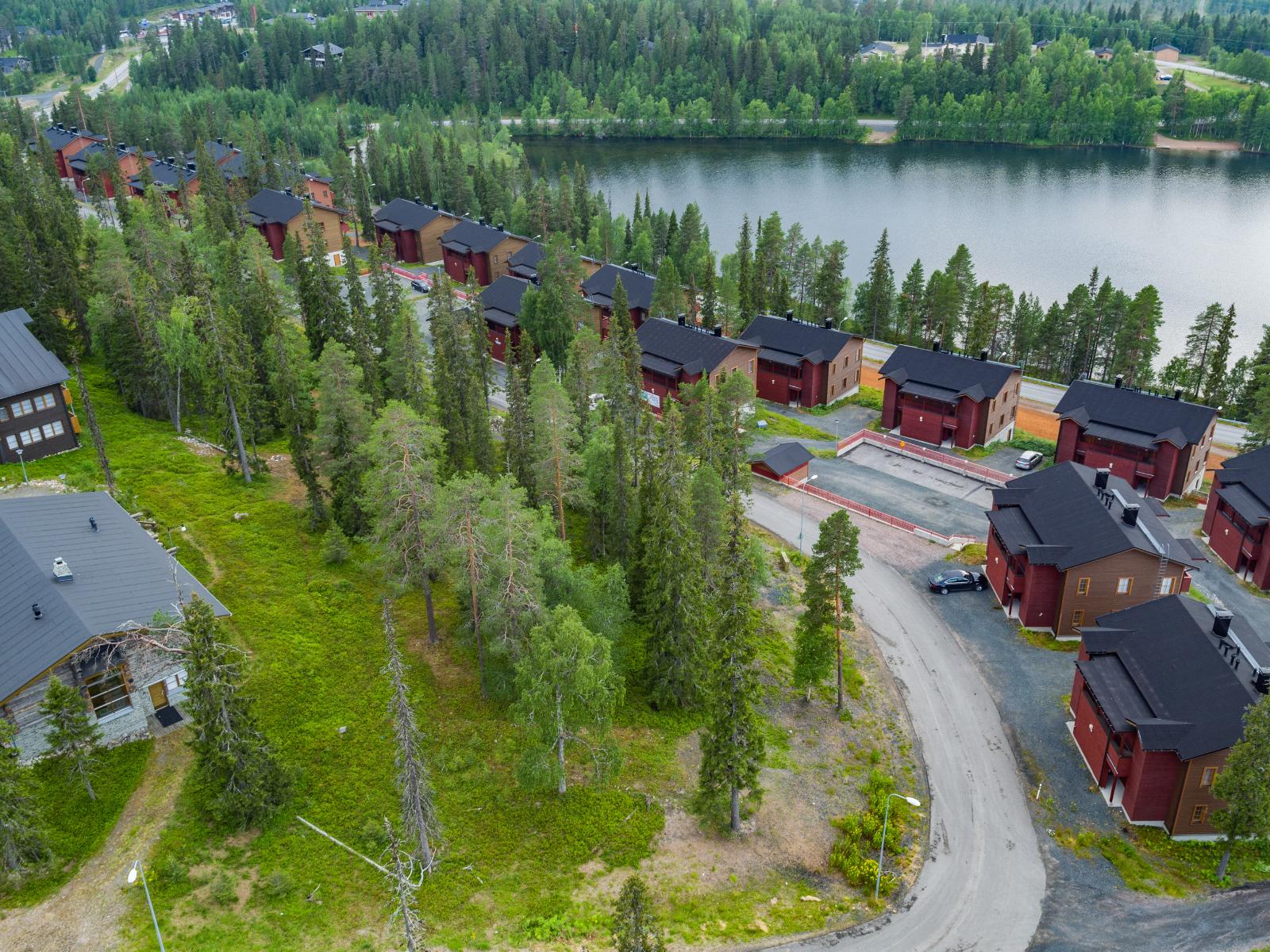 Järven läheisyydessä on lomahuoneistoja. Etualalla on havupuita kasvava kaistale. Ilmakuva.