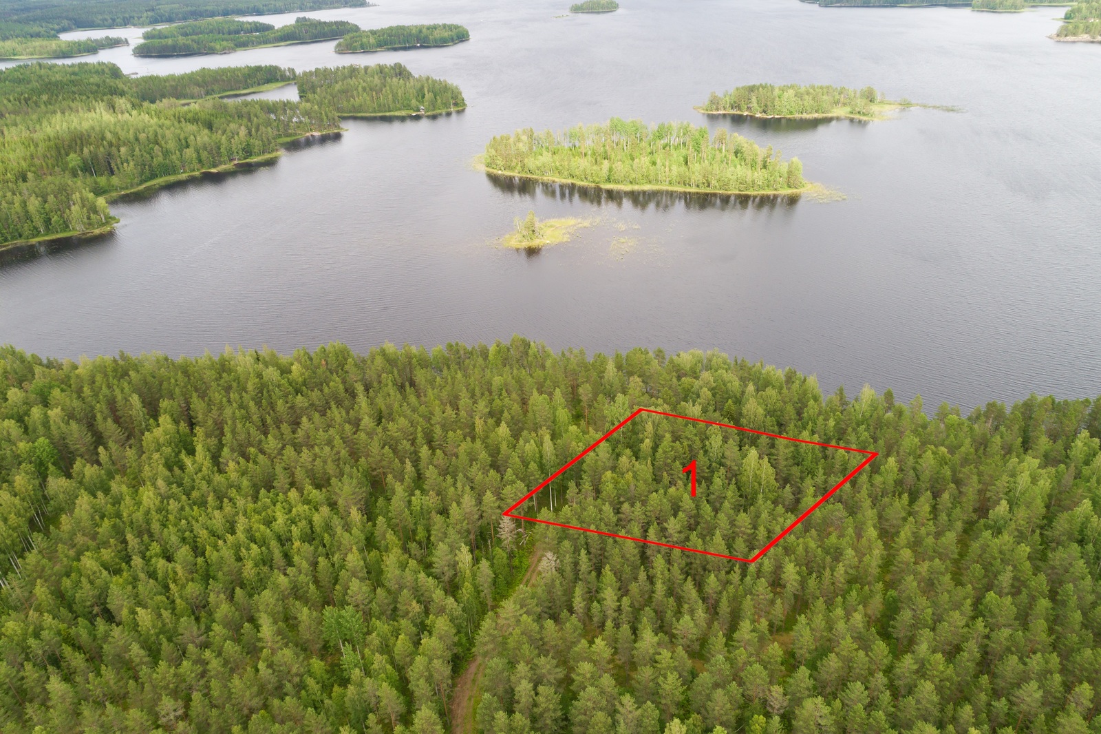 Ilmakuvassa piirrettynä tontin kaava metsän ylle lähellä rantaa. Järvessä on erikokoisia saaria.