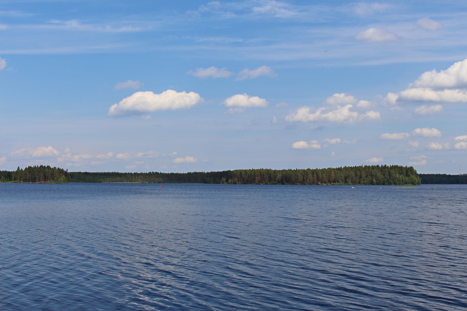 Laajassa järvimaisemassa puolipilvinen taivas heijastuu hieman väreilevään veteen.