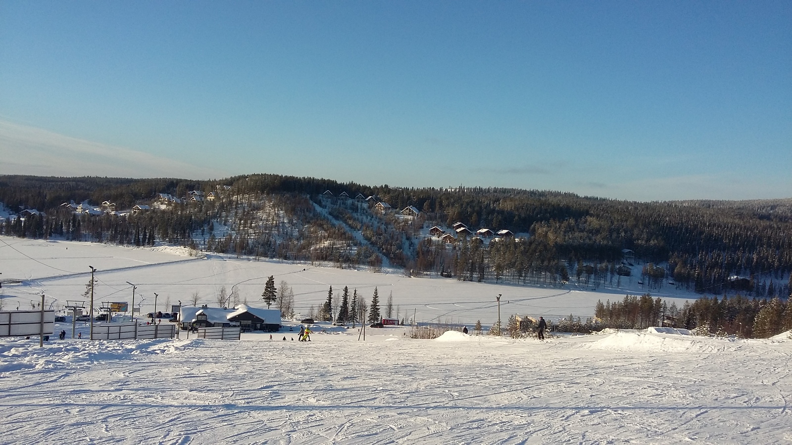 Laskettelurinteistä avautuu talvinen maisema järvelle. Vastarannan rinteessä on mökkejä.