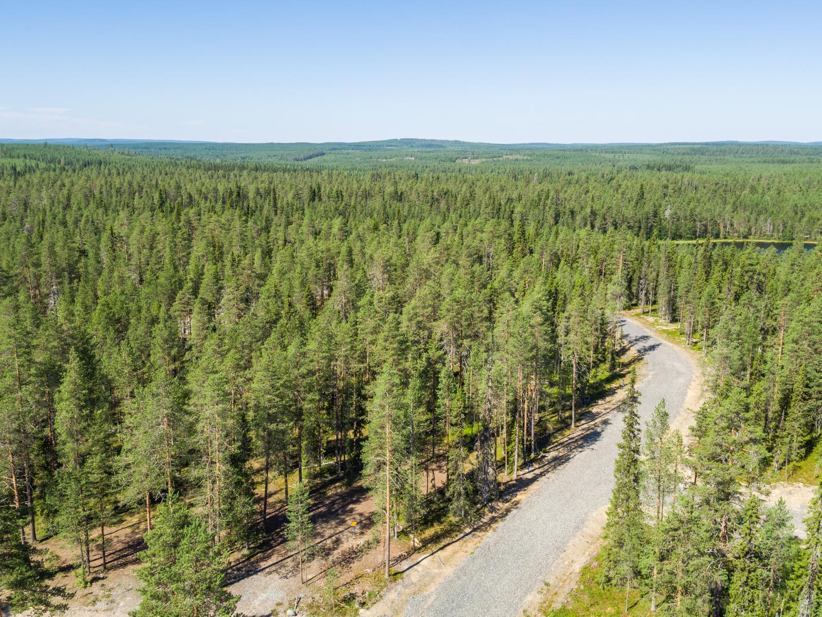 Ilmakuvassa tie haarautuu havumetsässä. Oikealla on vesistö ja horisontissa kumpuilevaa maastoa.