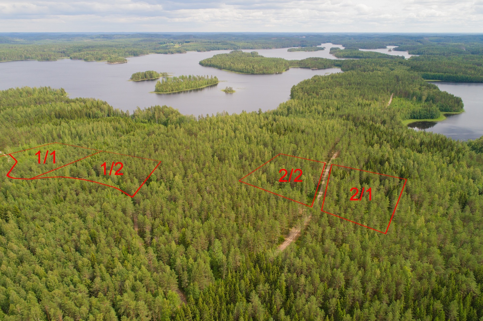 Ilmakuvassa piirrettynä neljän tontin kaavat metsän ylle. Vesistö reunustaa laajoja metsäalueita.